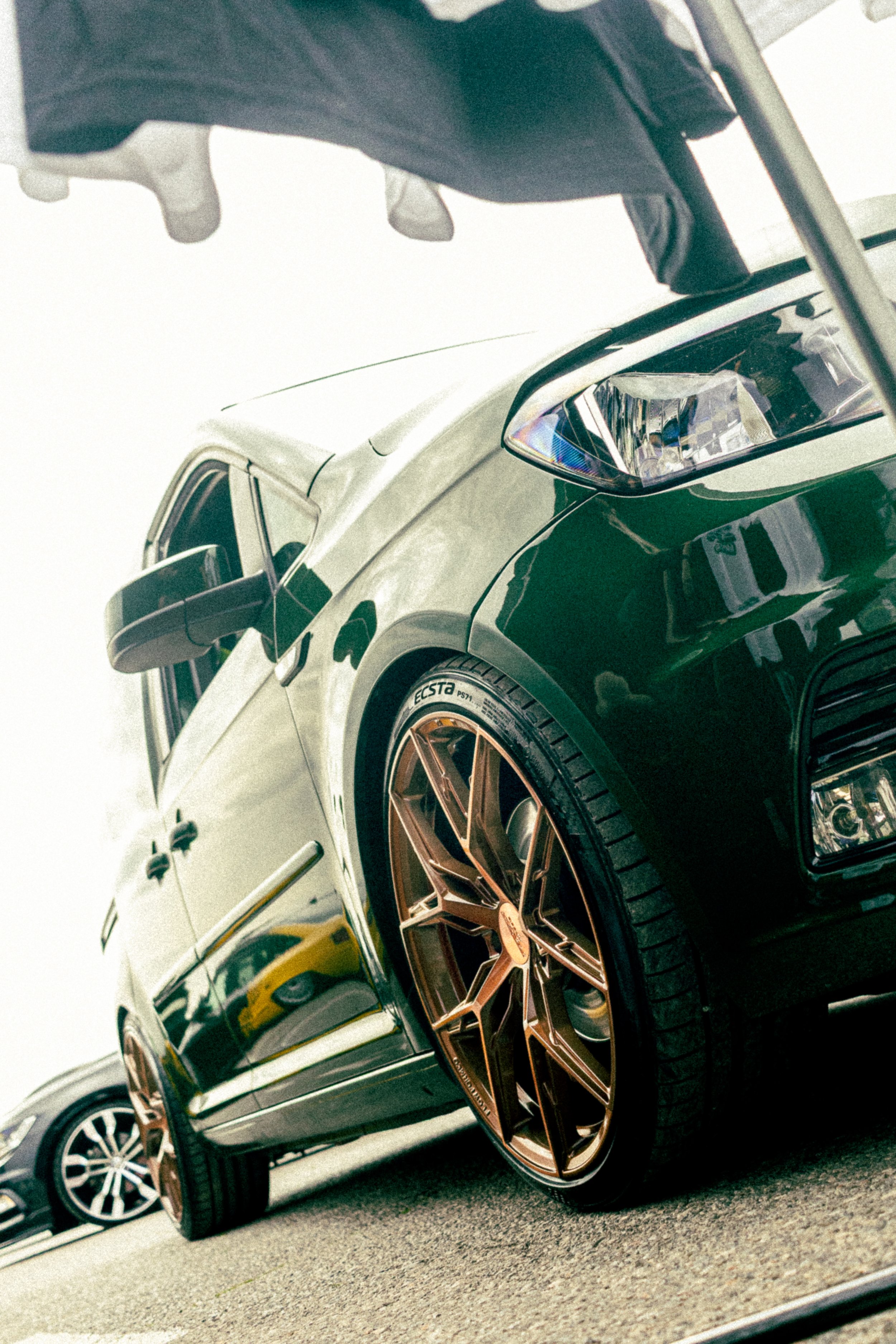 A row of cars parked at a dealership or parking lot, featuring a black vehicle with bronze-colored rims in the foreground.