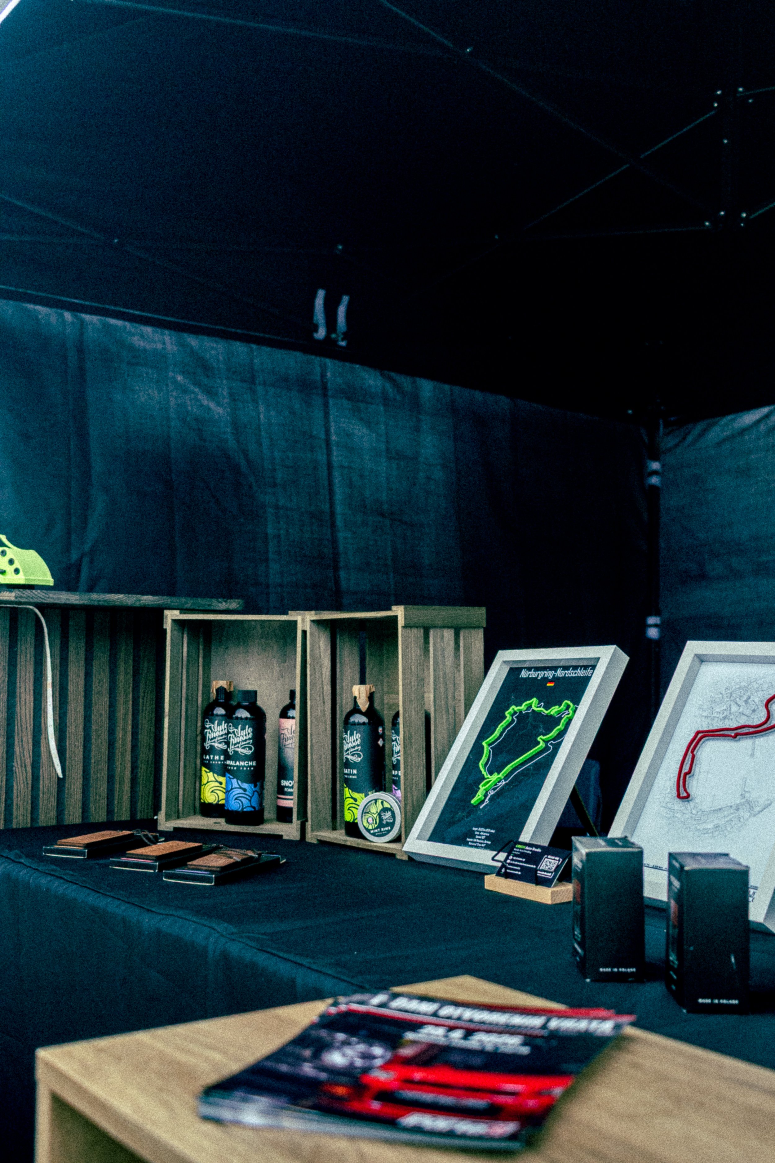 Table displaying various merchandise, including bottles, brochures, and framed artwork featuring a racing track map, set against a dark backdrop.