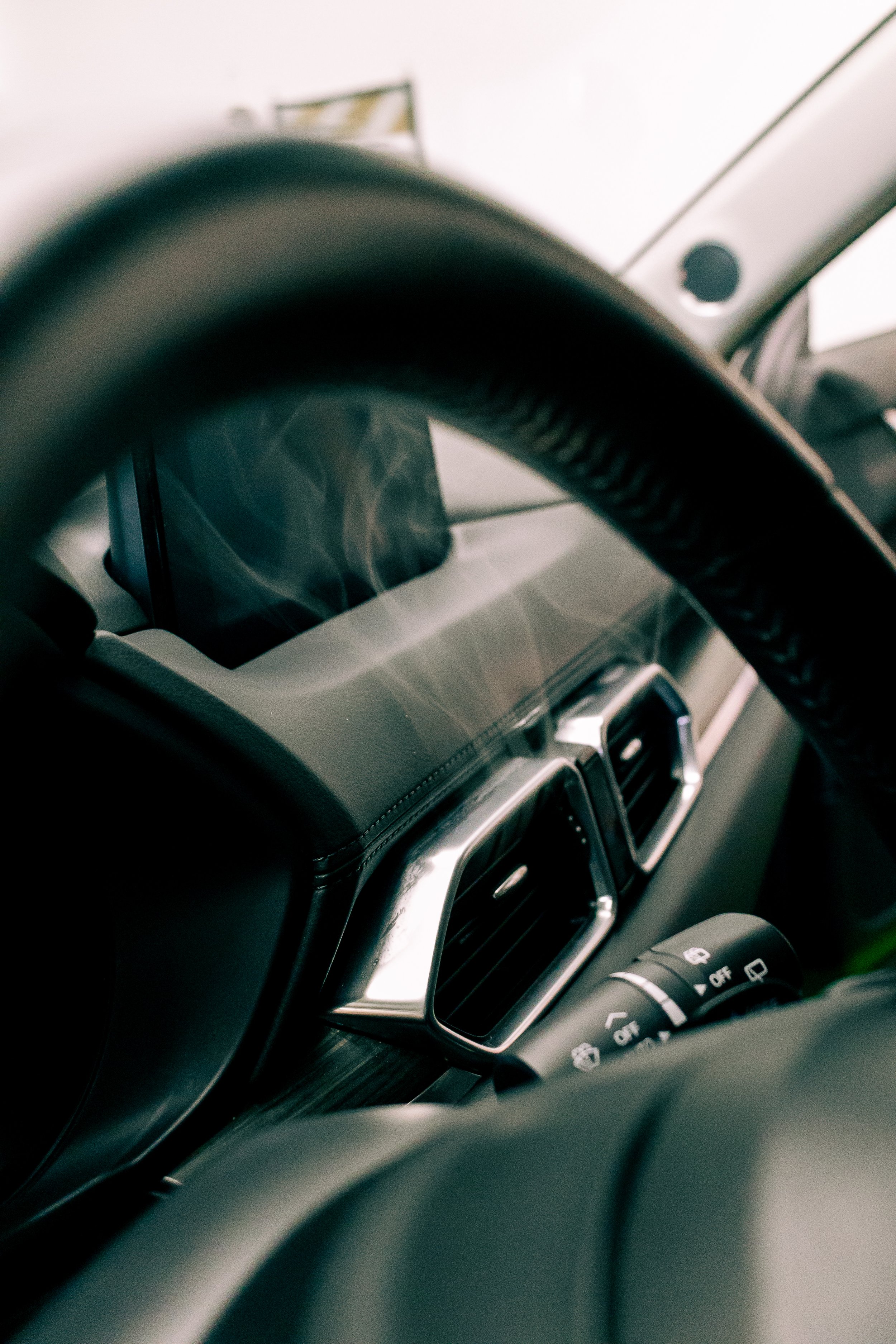 Close-up of a car's dashboard from the driver's seat, showing the steering wheel, infotainment screen, climate control buttons, and some of the windshield.