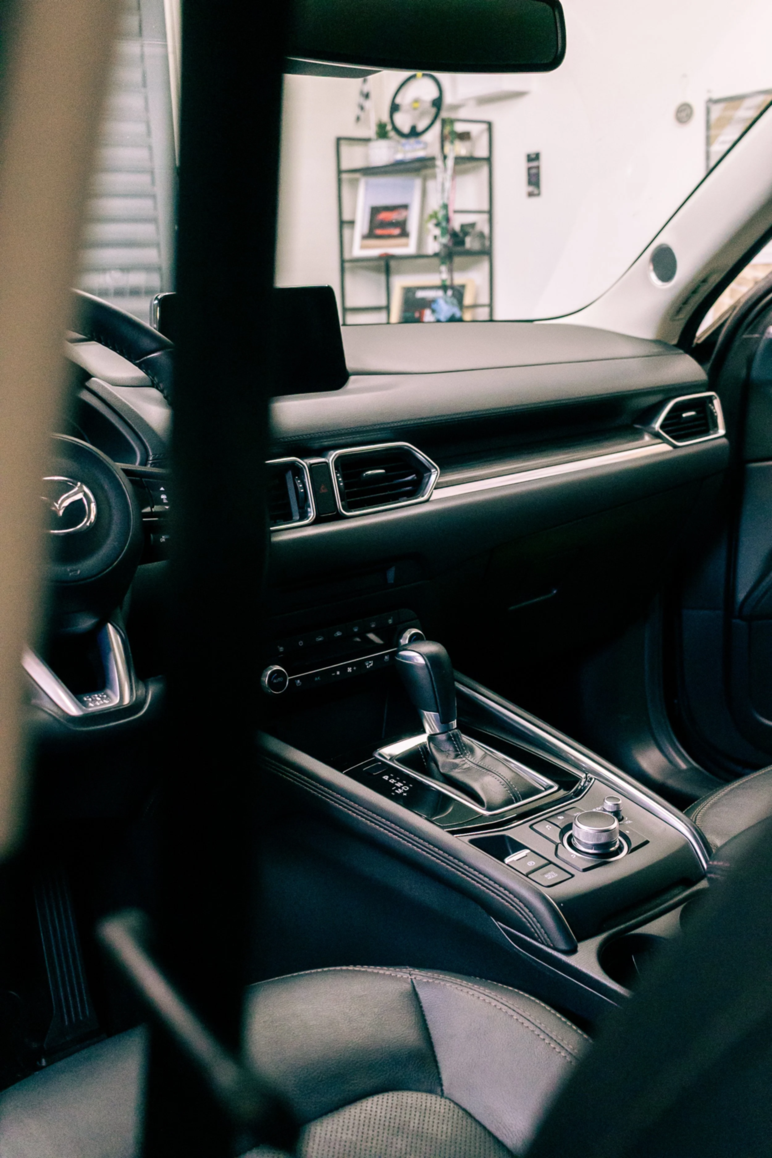 Inside view of a modern vehicle dashboard and center console, featuring an automatic gear shifter, rotary dial, and air vents, with a partial view of a steering wheel and seat.