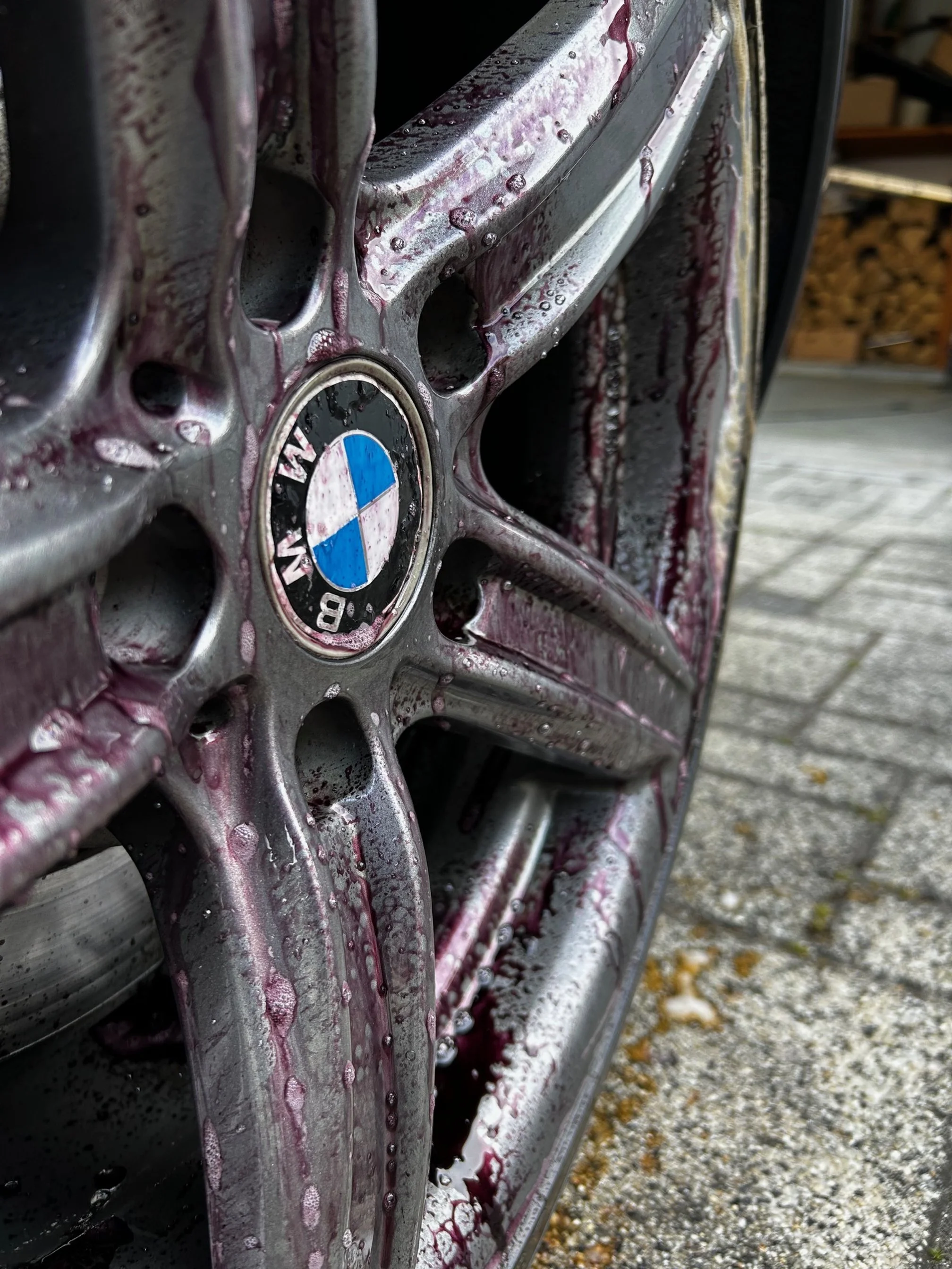 Close-up of a wheel rim with a BMW logo, covered in soap and water, on an outdoor surface.