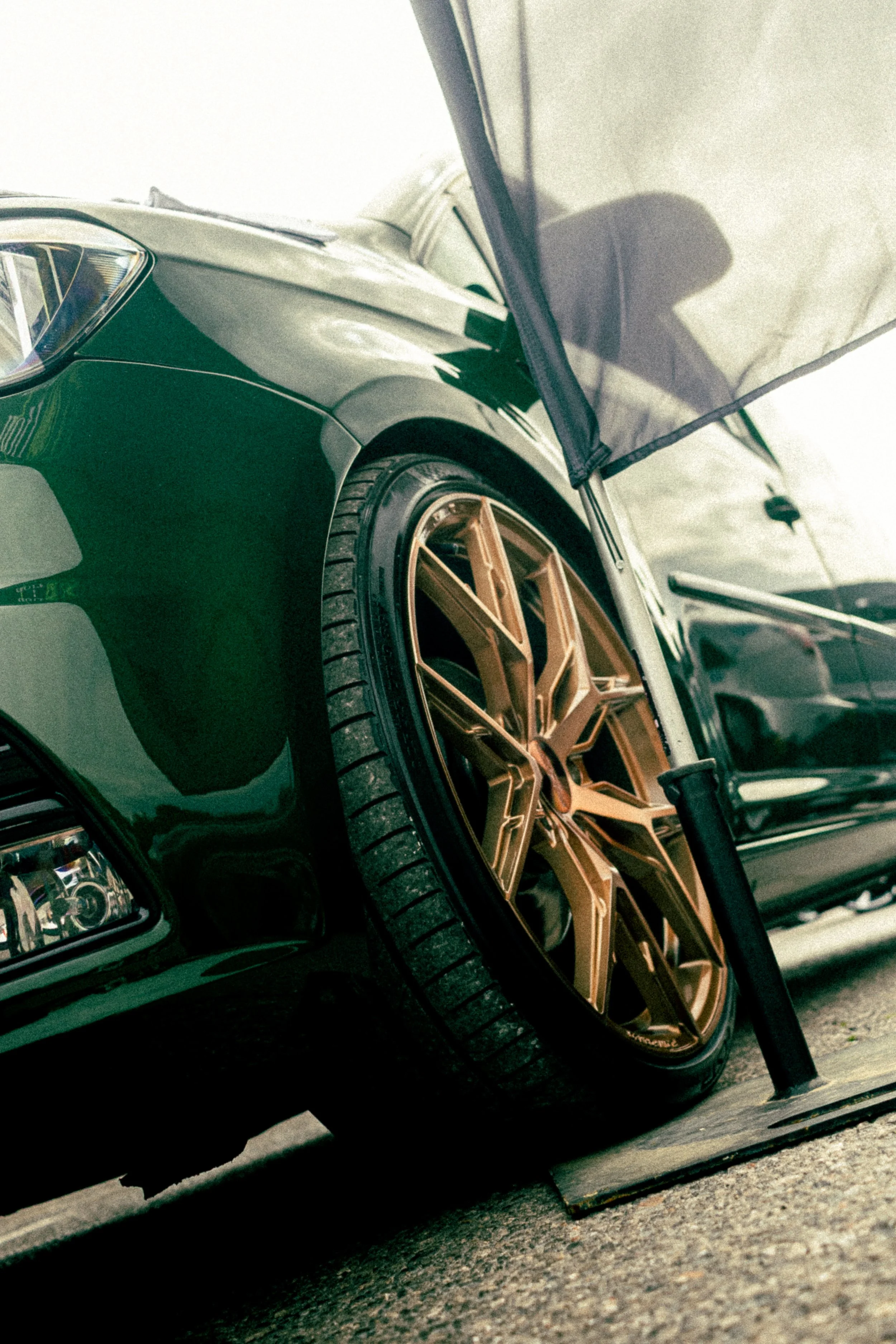 A close-up of a car with custom gold wheels parked on a street, with a parking curb and a concrete ground visible.