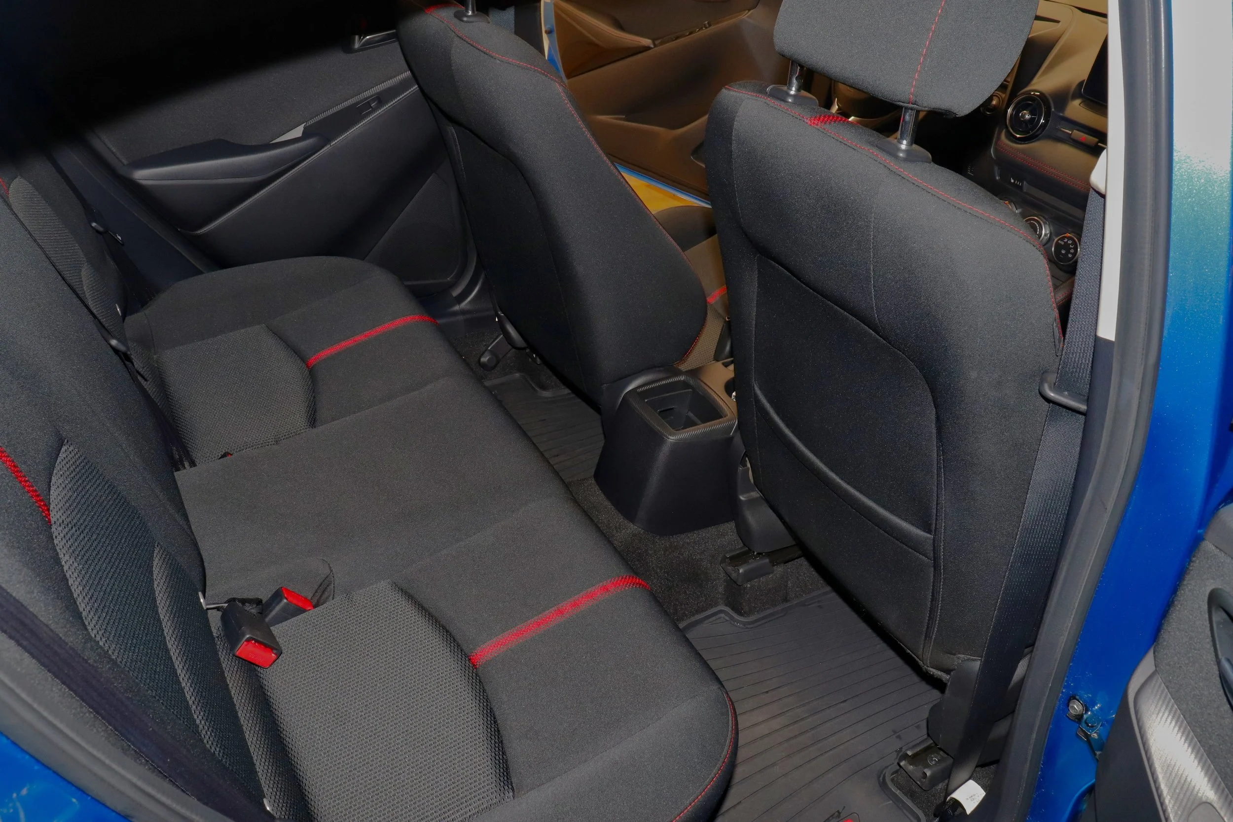 Car interior showing rear and front seats, black upholstery with red stitching, black floor mats, and open passenger door.