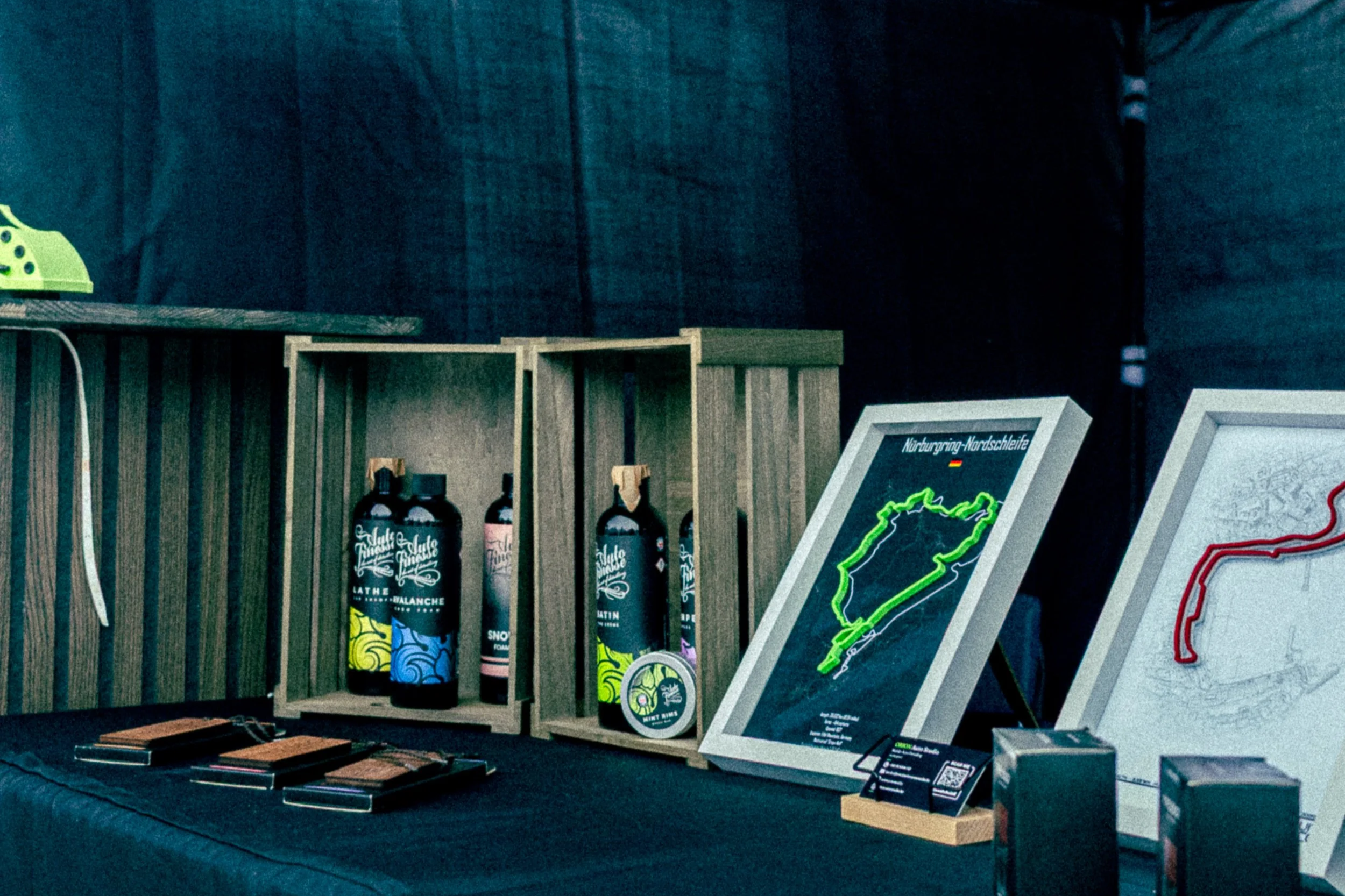 A display table with bottles of liquid and framed artwork, including a neon map outline of Italy, on a dark background.