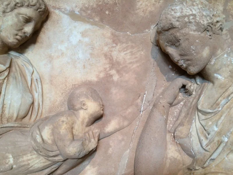 Detail from a funerary stele in the National Archaeological Museum of Athens. The mother (right) is the deceased. Her baby is pictured reaching eternally for the parent who is gone forever. Photo credit: Adam Groves / Ultreya Editorial