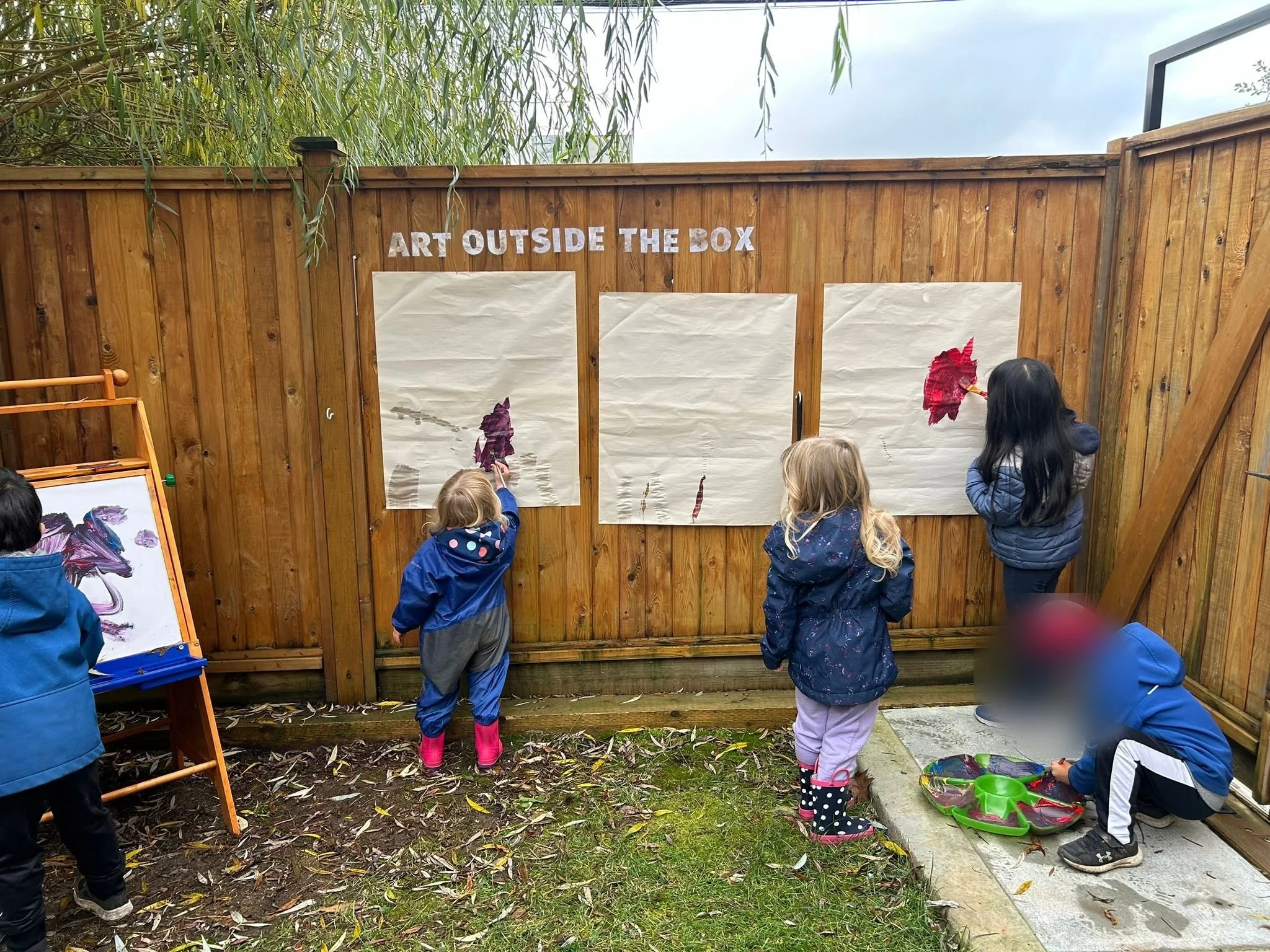 Children painting a fence at Green Valley Sunshine Kids daycare in Mission, BC