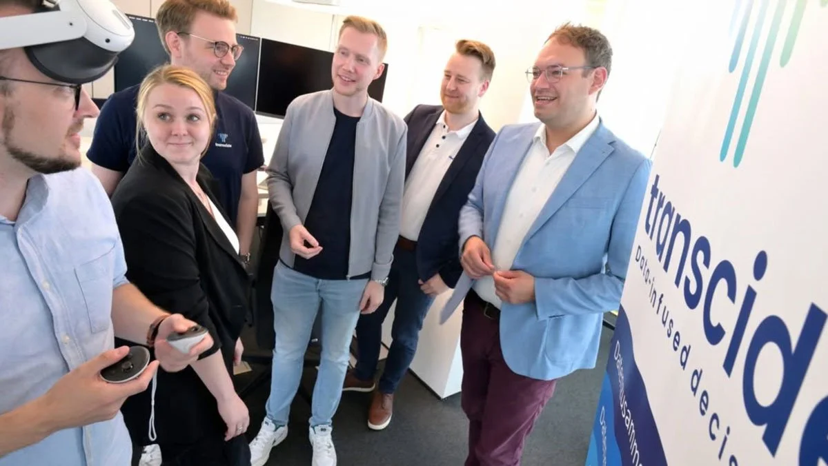 Eine Person mit VR-Brille im Vordergrund mit dem Team von transcide und dem Landtagsabgeordneten Stephan Christ auf dem Messestand in Emstek.