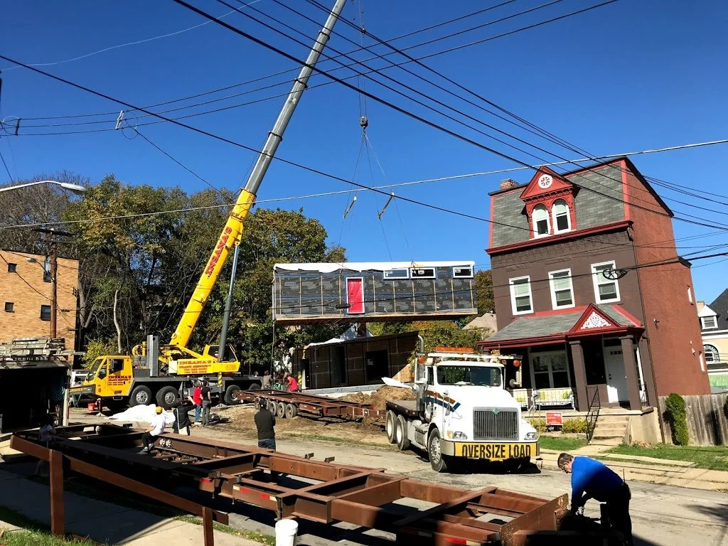 An image of a crane setting down a newly built home designed by FormWright Design, Aurora McClain Architect