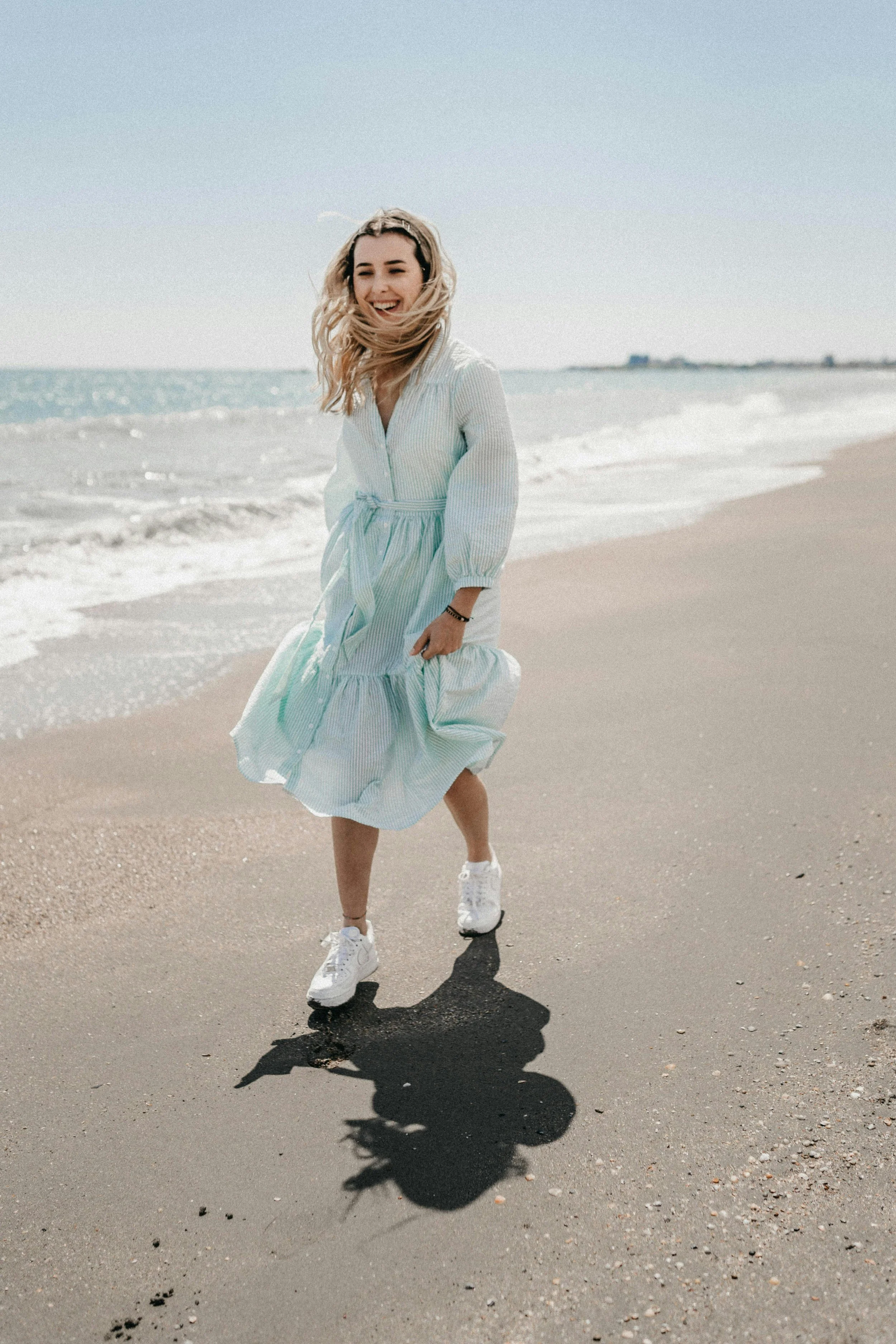 Girl smiling and running along the Tampa, FL coastline in a billowing dress, hair blowing in the wind, evoking joy and freedom