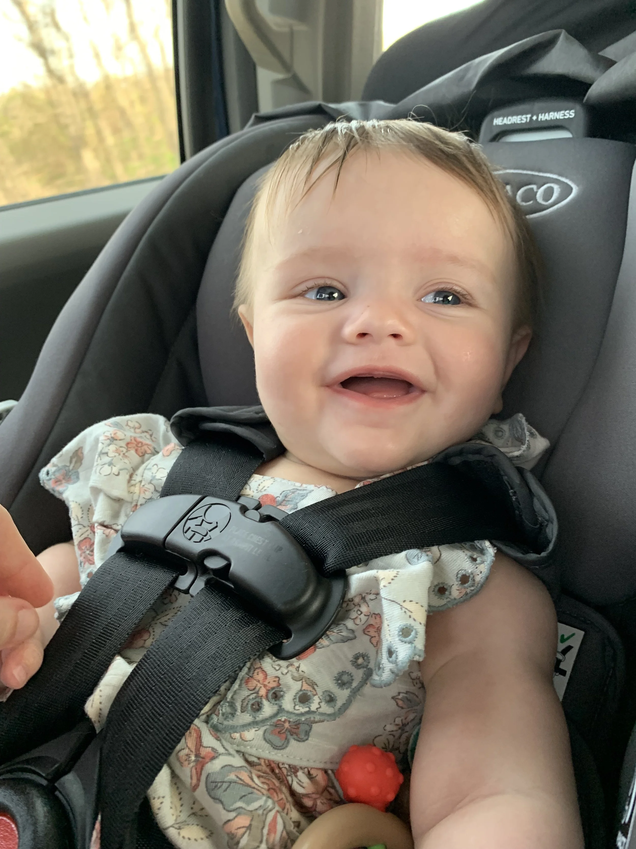 a baby in her car seat smiles.