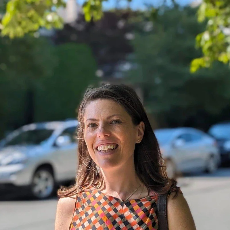 Sophé, smiling outdoors with trees and parked cars in the background.