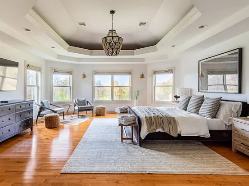Bright bedroom with a large bed, multiple windows, and a seating area with chairs and a rug.