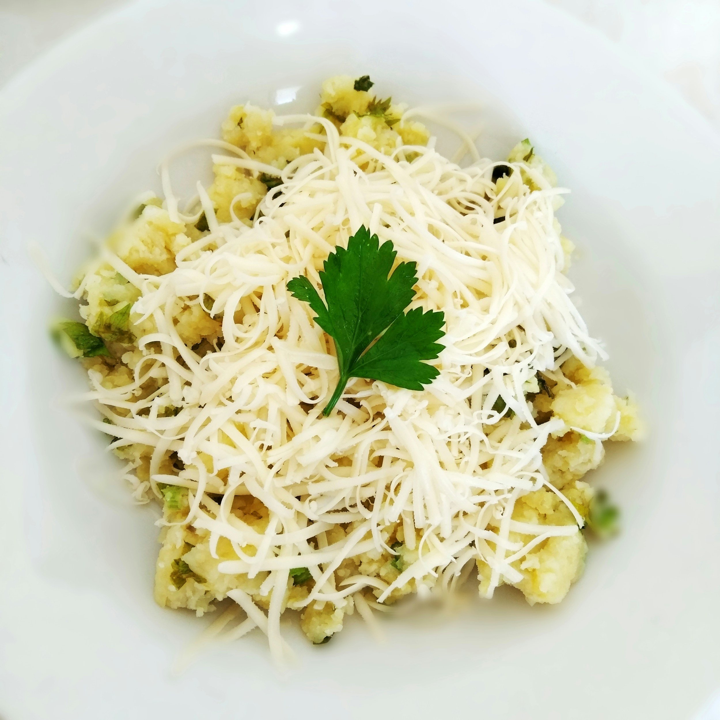 Cauliflower florets topped with shredded cheese and a sprig of parsley in a white bowl.