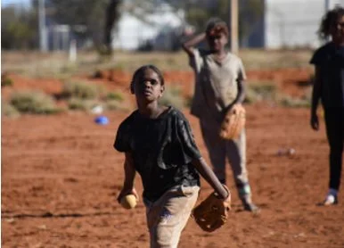 Children playing baseball outdoors on a dirt field.