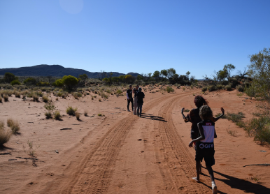 Group of hikers walking on a dirt trail in a desert landscape with sparse vegetation and distant mountains on a clear, sunny day.