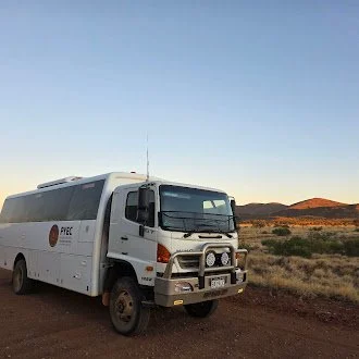 A white mobile medical clinic vehicle parked on a rural dirt road with a desert landscape and mountains in the background.