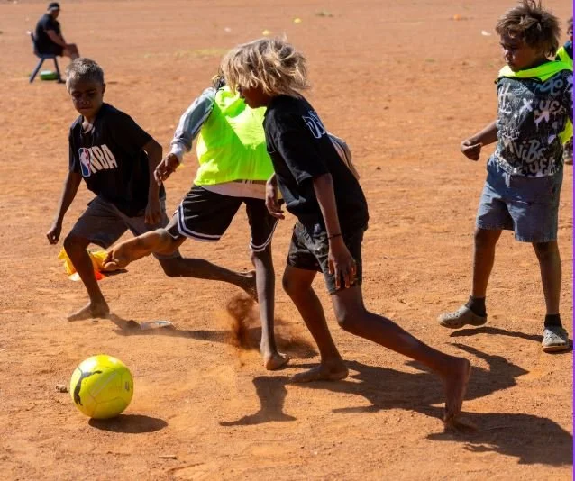 Children playing soccer on a dirt field