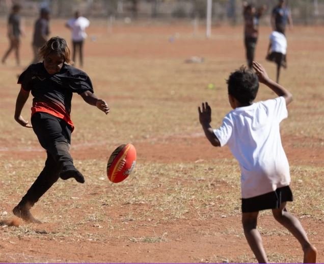 Children playing rugby on a dry, open field during daytime.