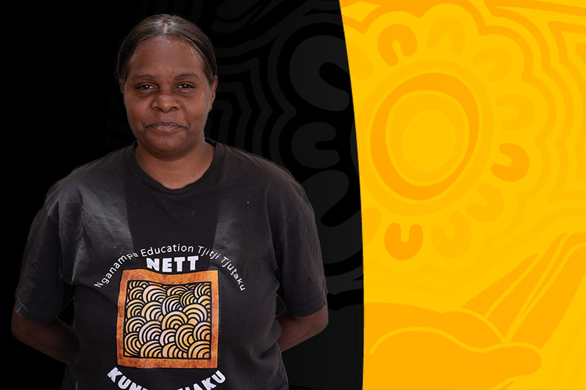 A woman standing in front of a background divided into black and yellow sections with an abstract sun design. She is wearing a black T-shirt that has a logo with a square pattern and text that reads 'Nanampa Education Titiji Tuutaku NETT KUNAPAKU'.