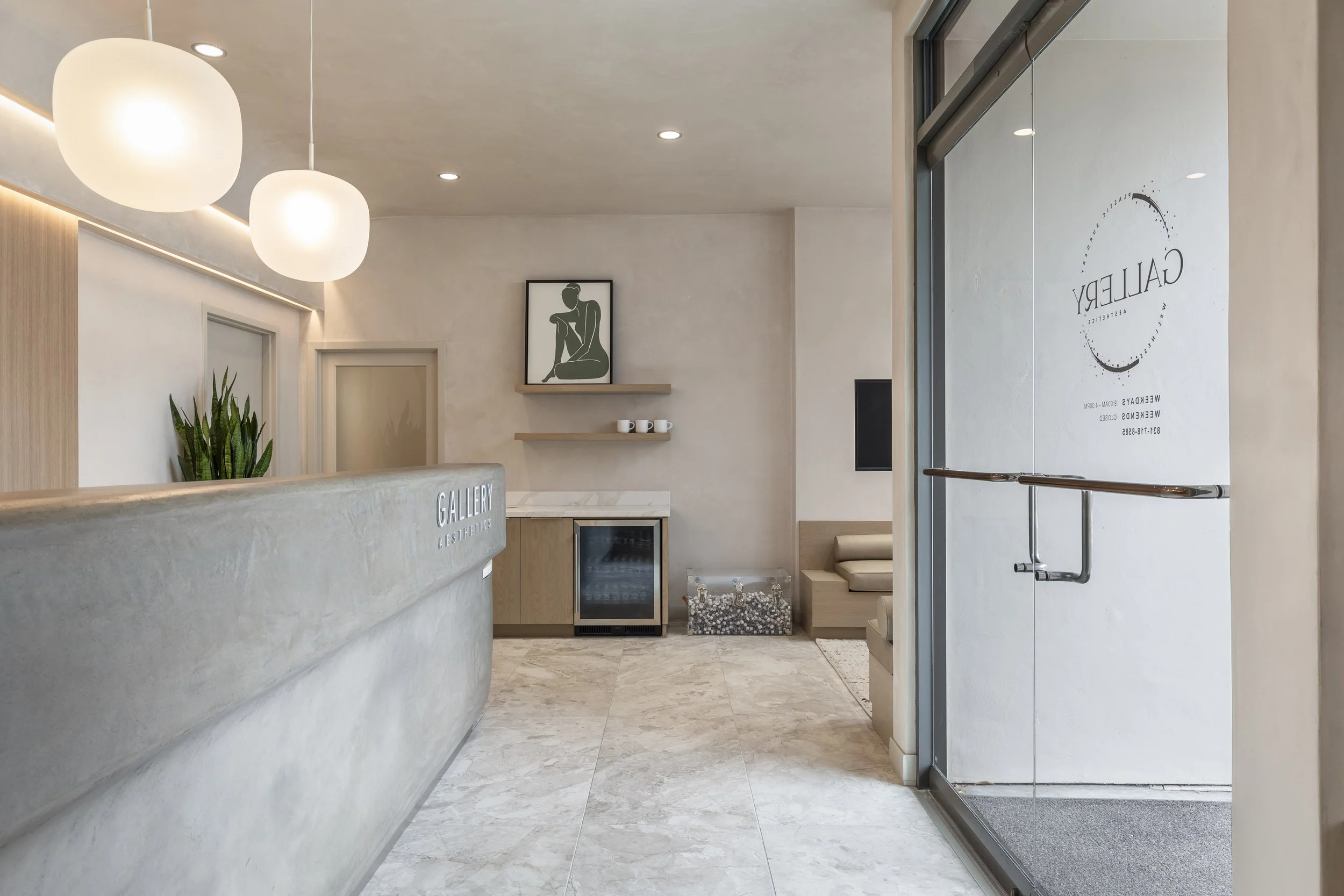 Plastic surgical office lobby featuring frosted light pendants, a curved concrete reception desk.