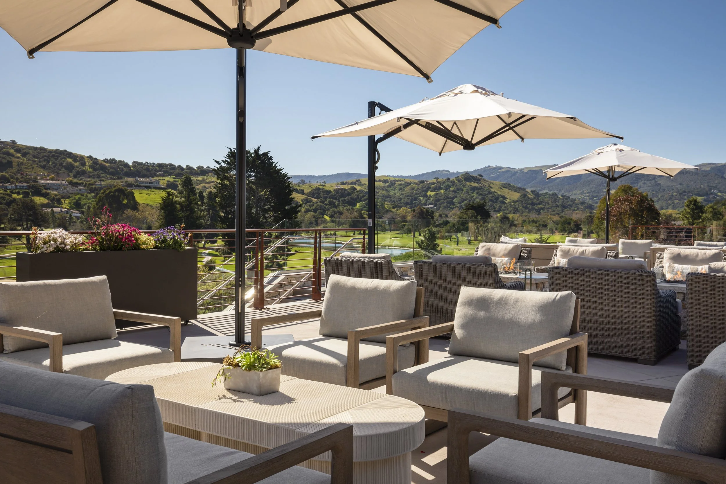 A scenic outdoor patio with comfortable seating, umbrellas, and a stunning view of rolling hills and a golf course.