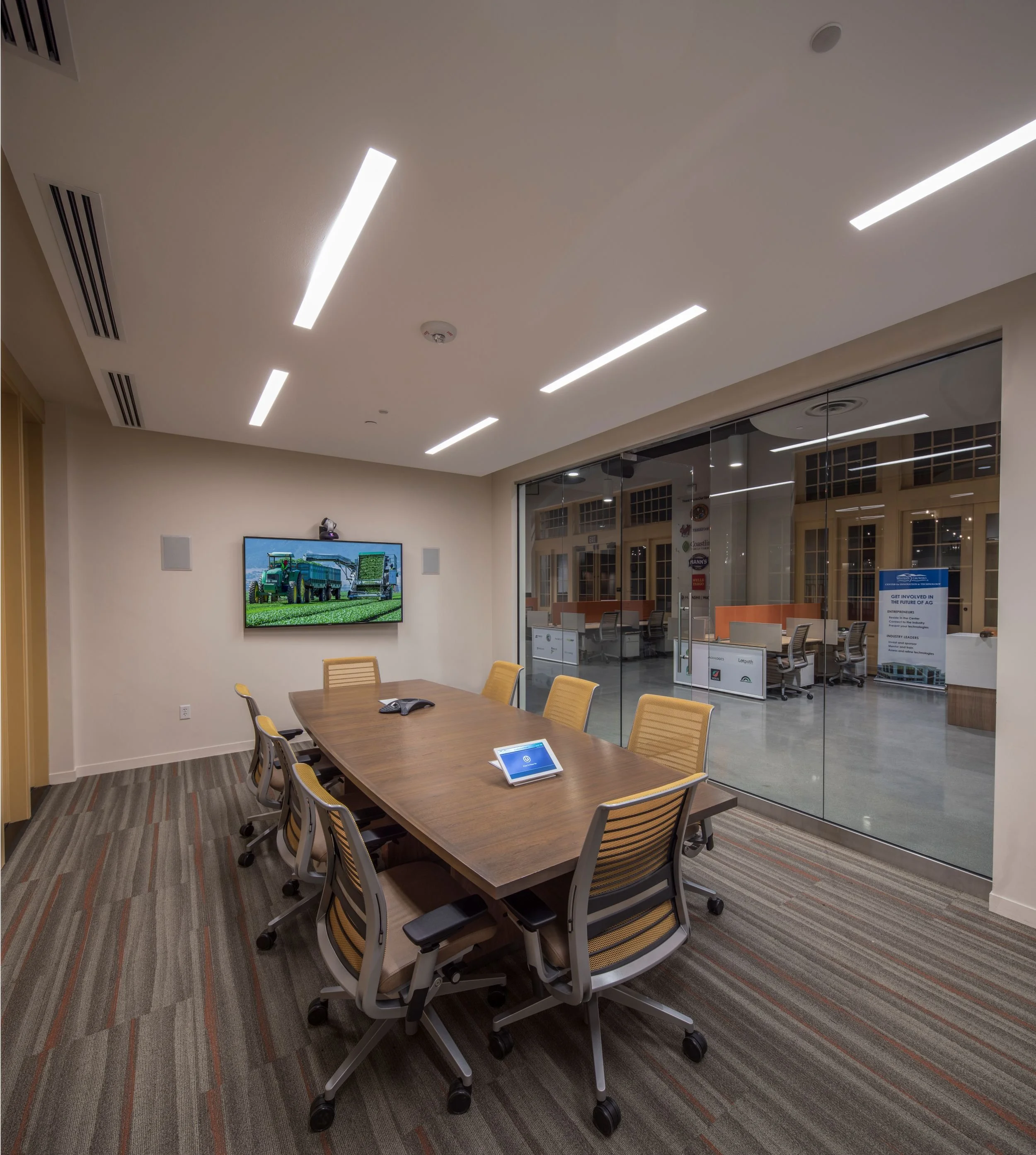 Conference room with a wood conference table, seating, and TV monitor. Interior storefronts allow visibility into the open office.