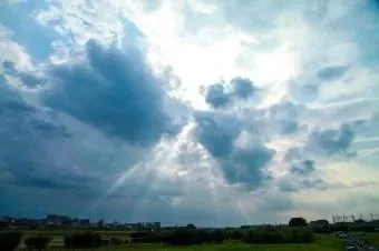 Cloudy sky with sunlight rays breaking through clouds over a grassy landscape.