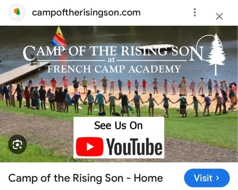 A group of children and adults holding hands in a circle on a grassy area by a lake with a dock and a colorful flag. Text overlay reads "Camp of the Rising Son at French Camp Academy" and a YouTube logo with "See Us On".