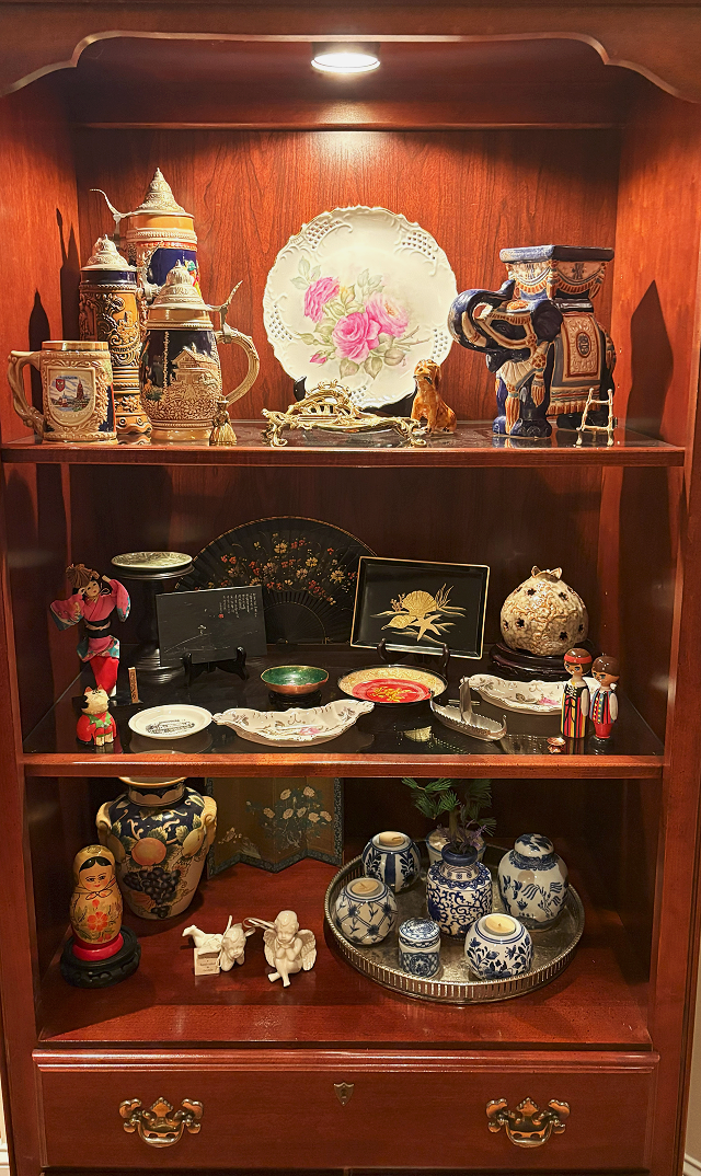 A wooden display cabinet with three shelves holding Asian and vintage decorative items.