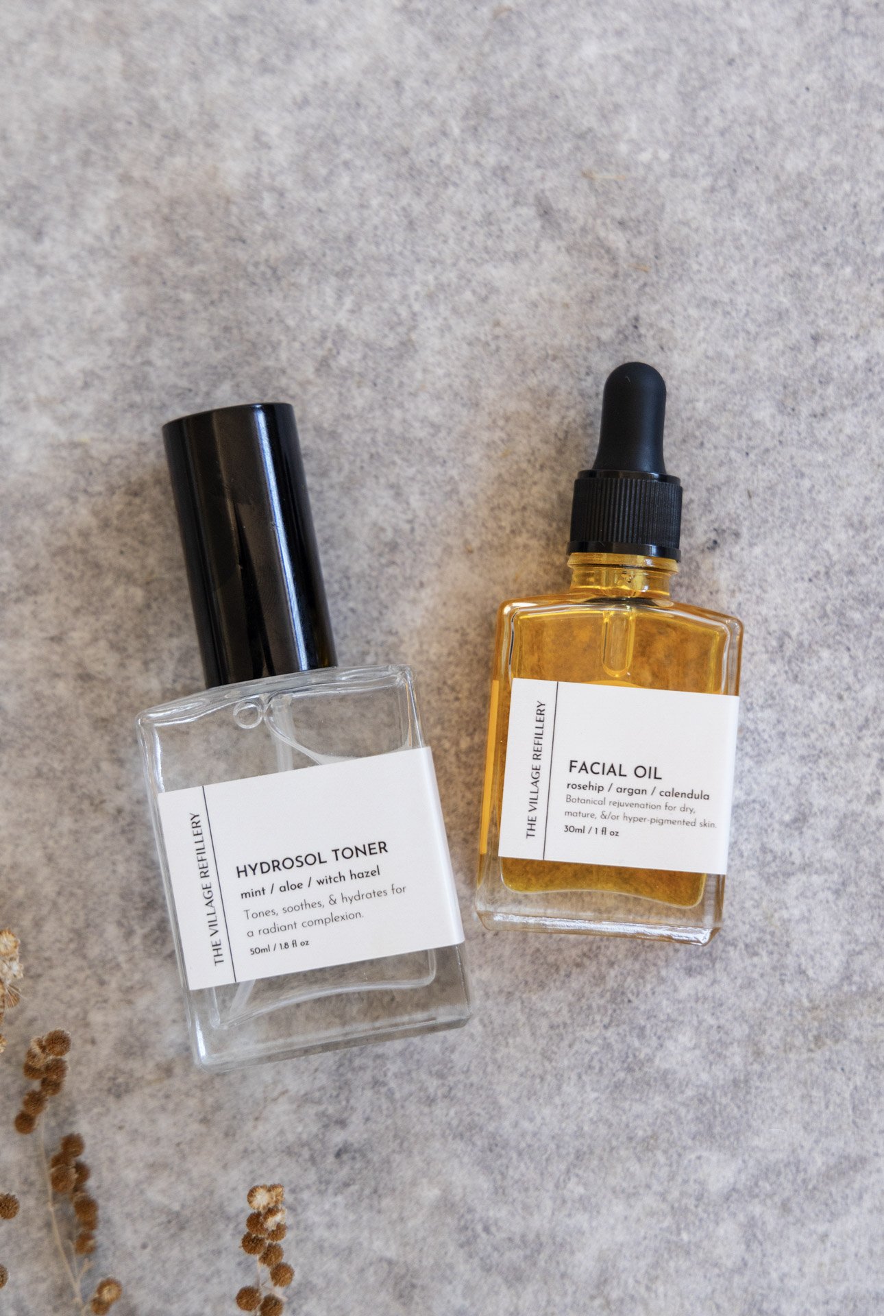 glass atomizer spray bottle and glass dropper bottle with white label and black text reading "hydrosol toner" and "facial oil" respectively