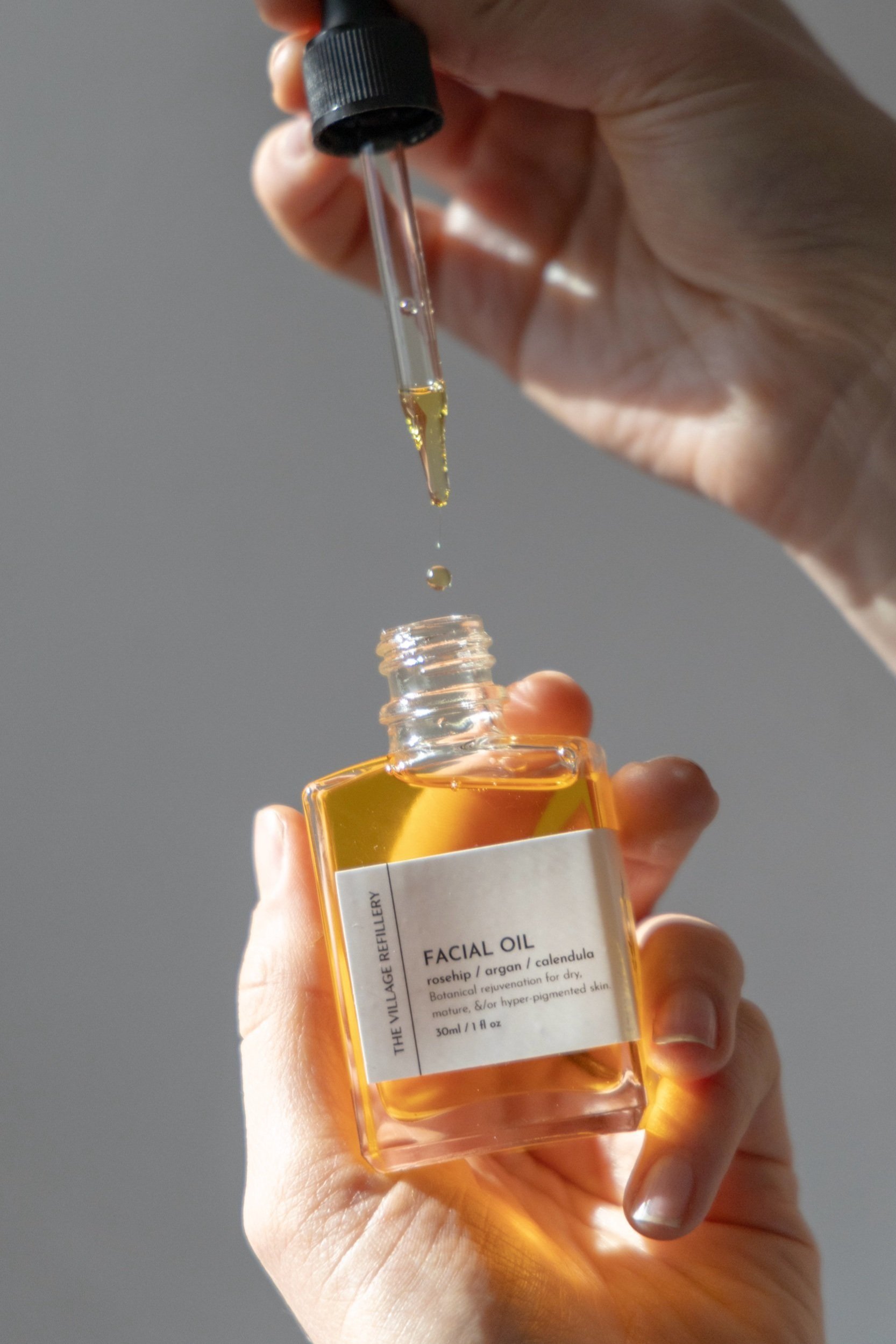 glass dropper bottle with white label and black text reading "facial oil" bottle is opened and dropper is being used to show its function