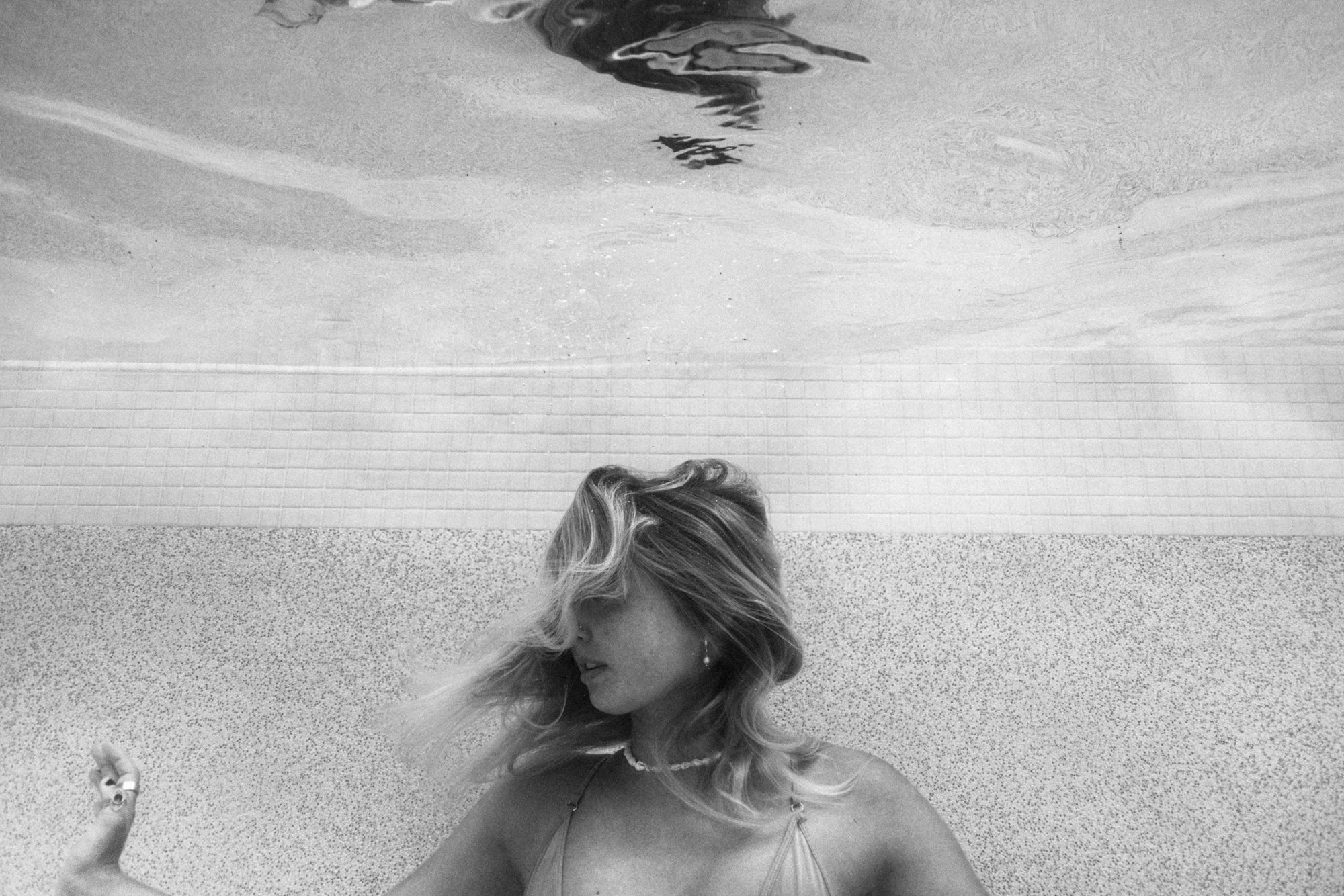 Woman underwater, black and white, hair flowing, wearing earrings and necklace.