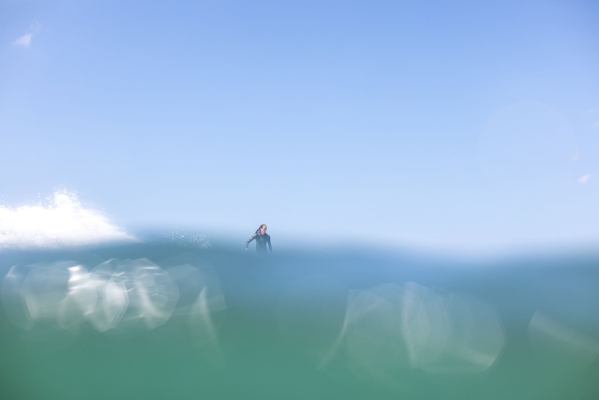 A person surfing on a wave in the ocean under a clear blue sky.
