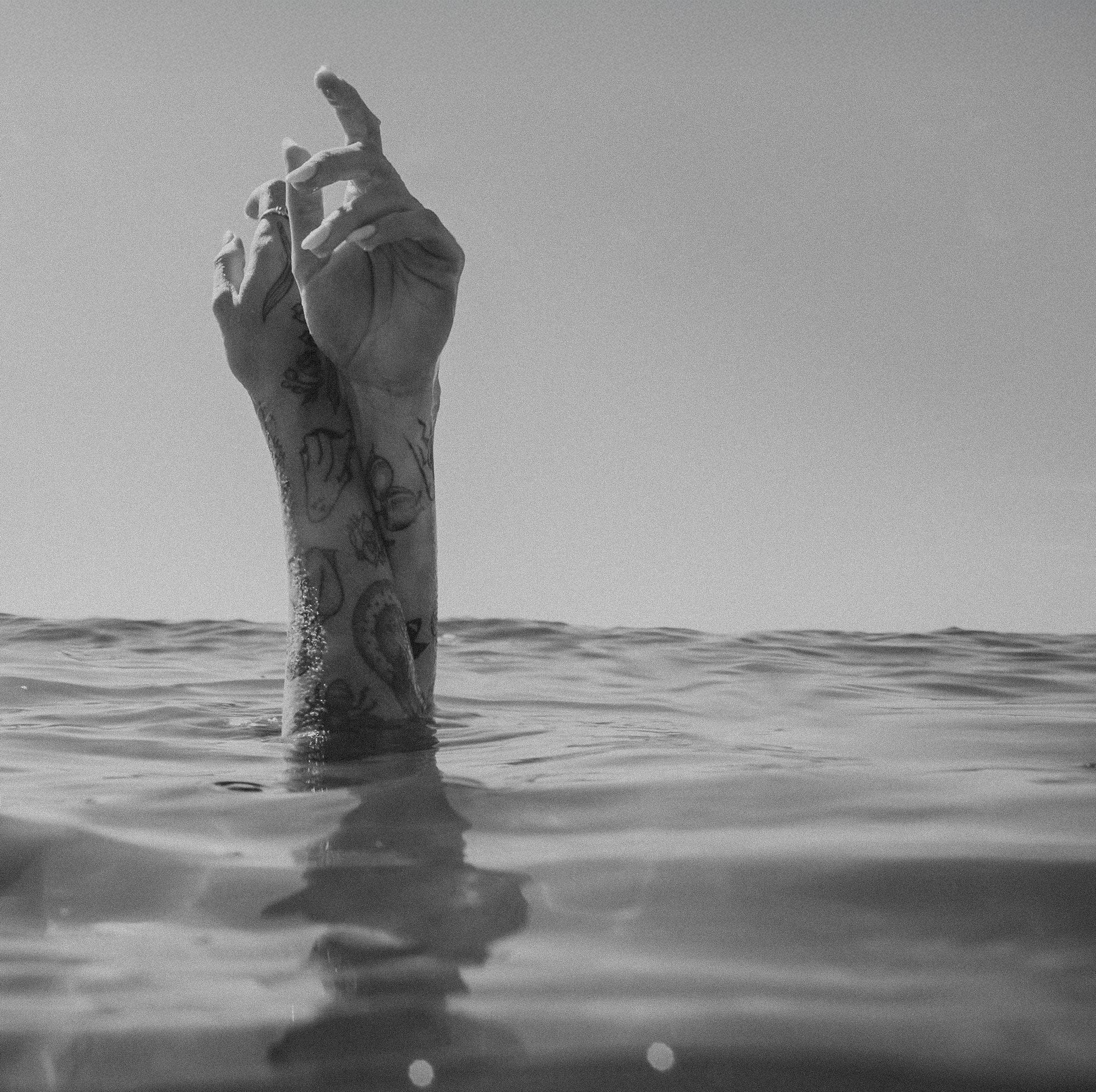 Tattooed hand raised above water surface in black and white