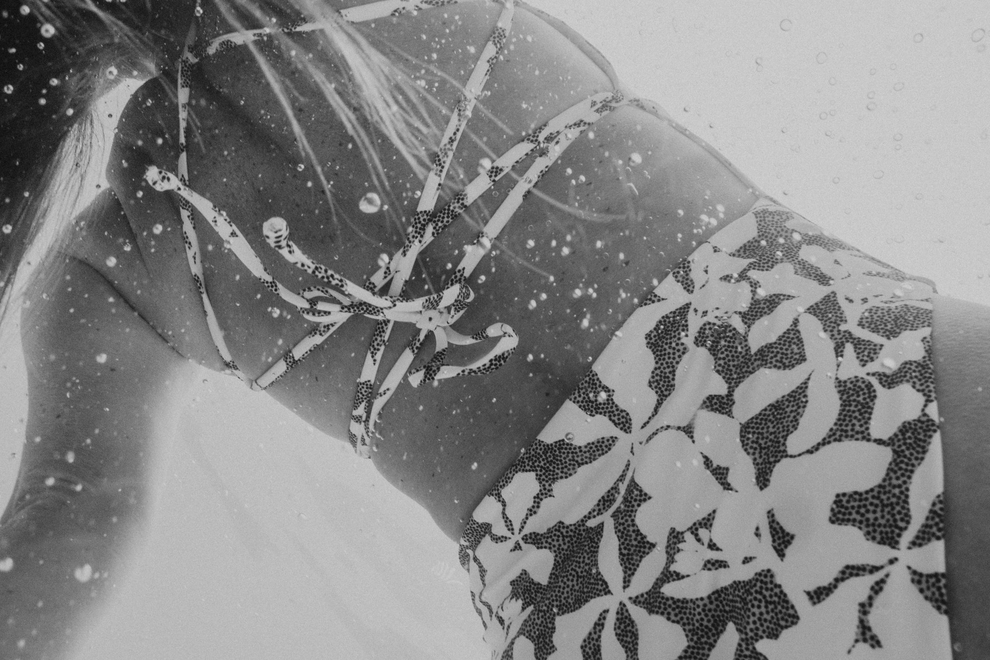 Woman wearing tropical patterned swimwear under water, with water droplets around her.