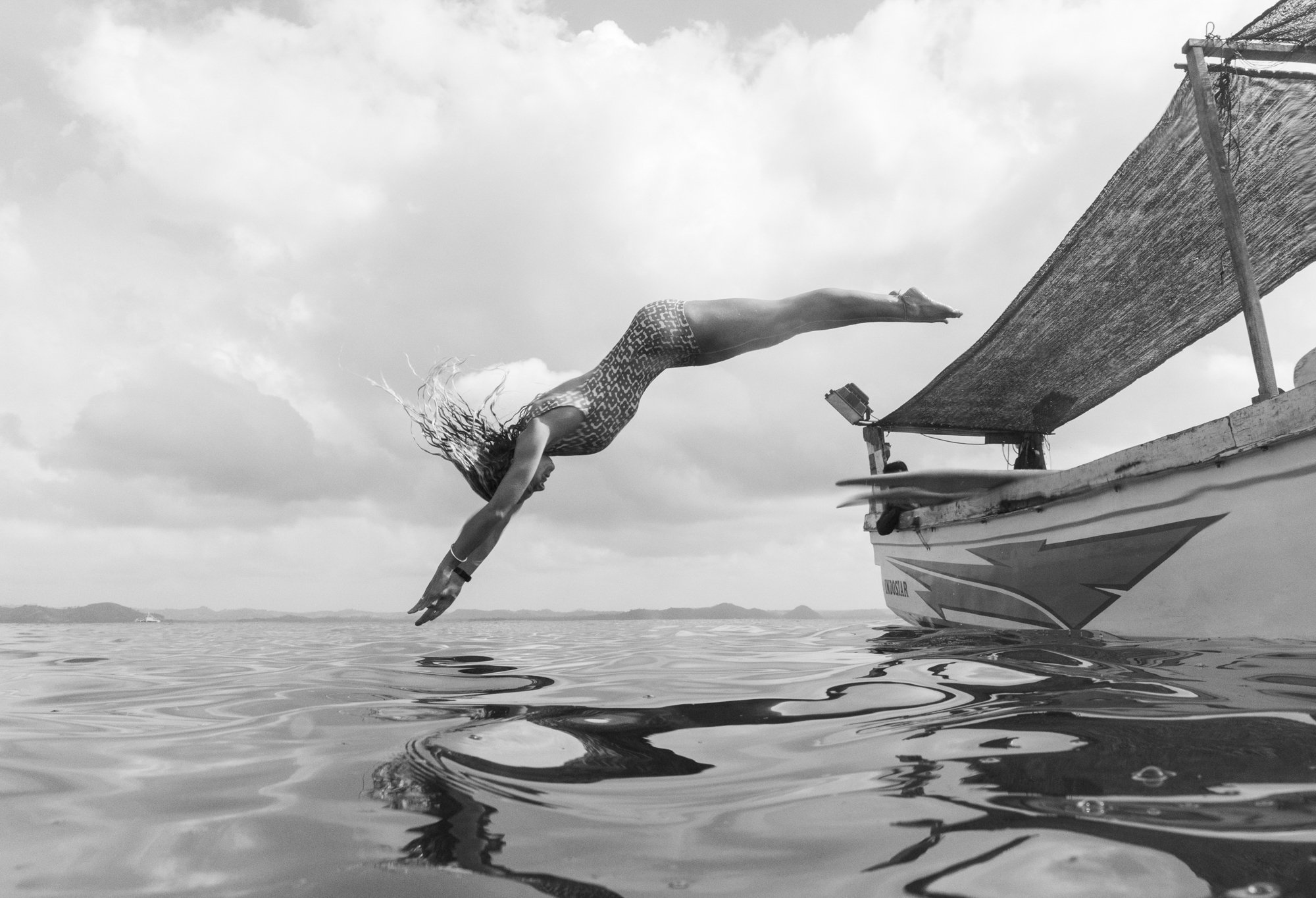 A woman in a swimsuit diving into the water from a boat on a cloudy day.