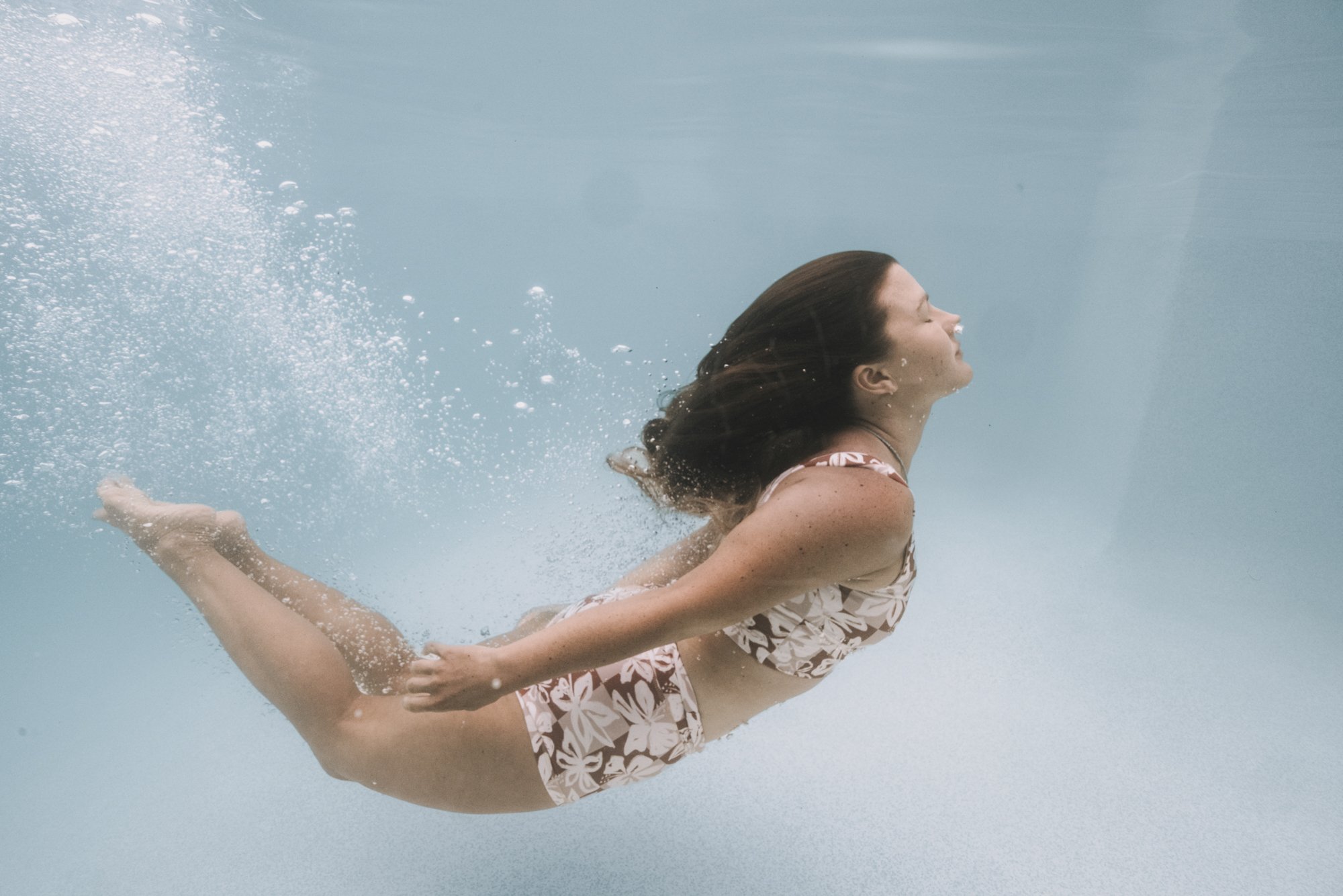 Woman swimming underwater in a pool wearing a floral bikini, with bubbles around her.