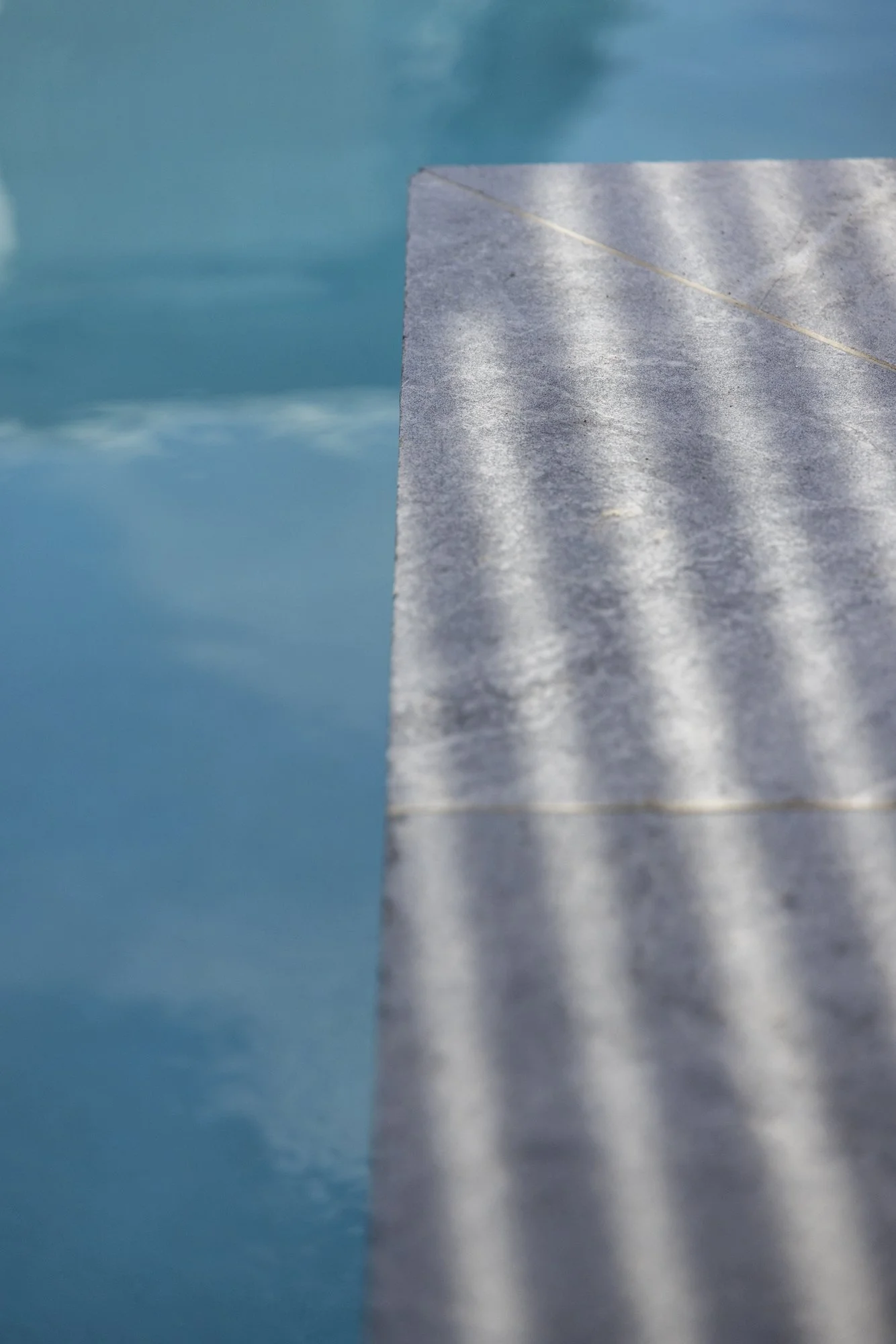 Close-up of a metallic diving platform against a blue swimming pool background.
