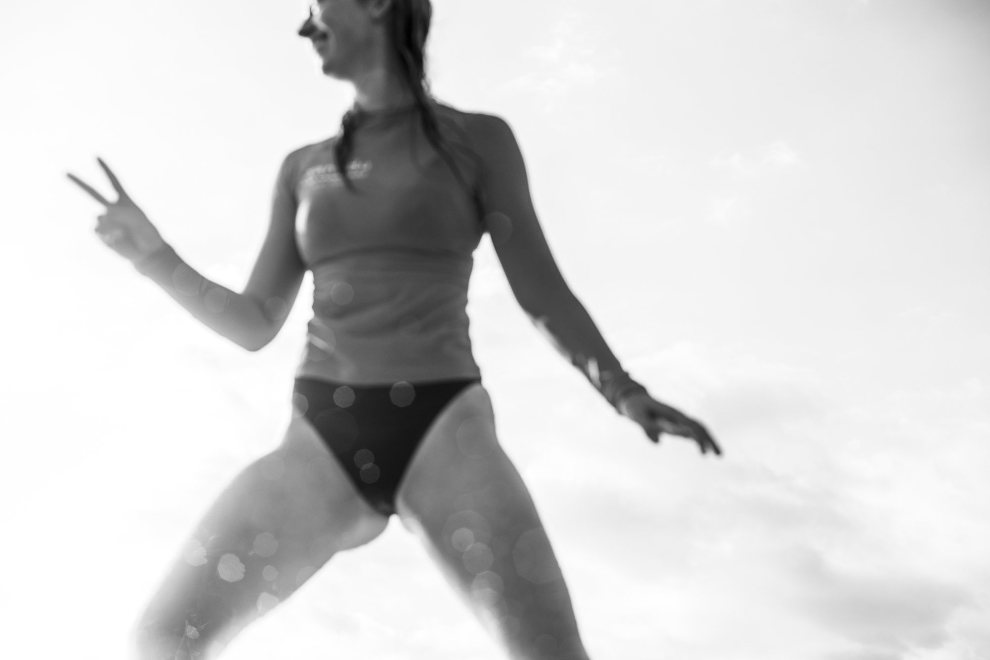 A woman in a bikini making a peace sign with her hand, standing outdoors against a bright sky.