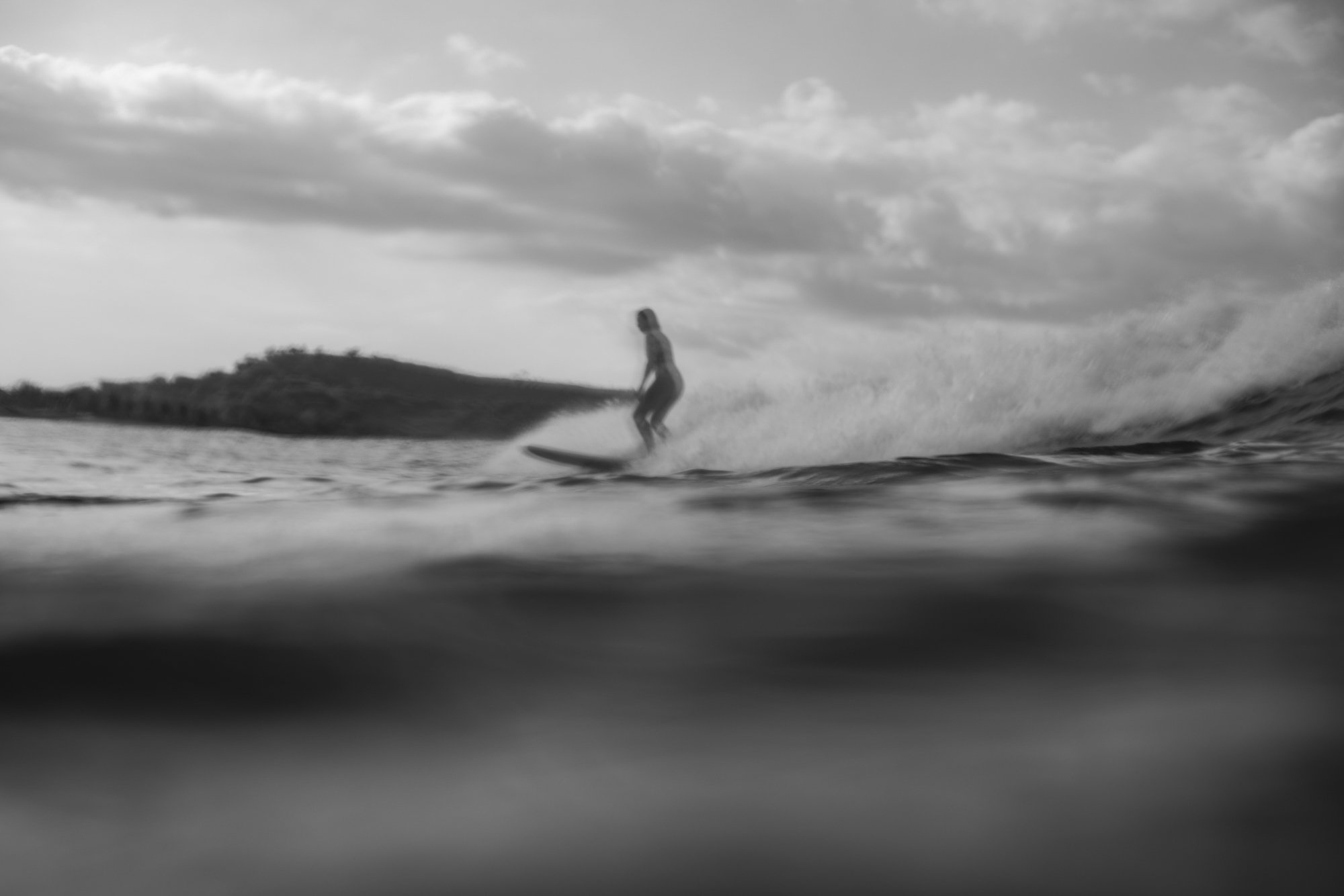 A person surfing on a wave in the ocean during cloudy weather, in black and white.