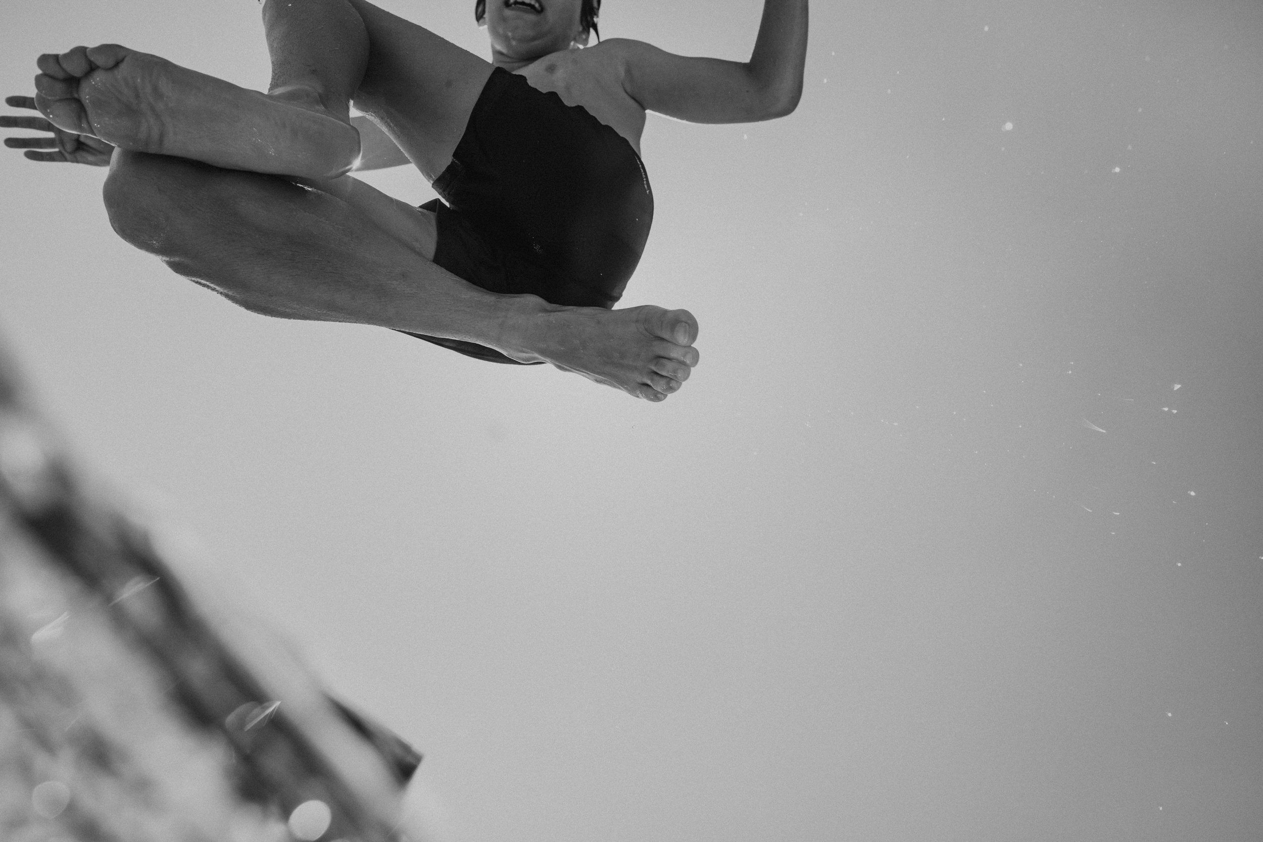 Child jumping in the air, with legs crossed and arms raised, against the sky in black and white.