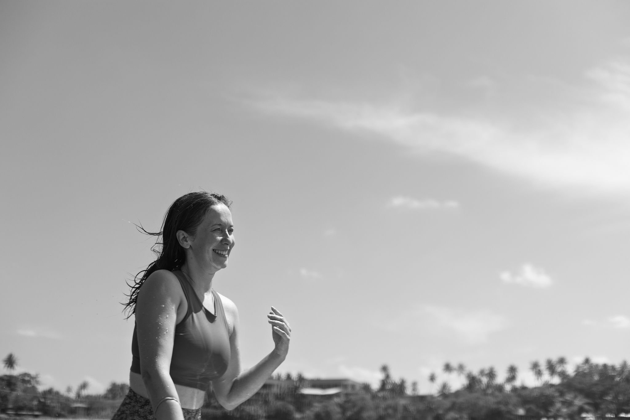 A woman smiling and running outdoors on a sunny day with palm trees in the background.