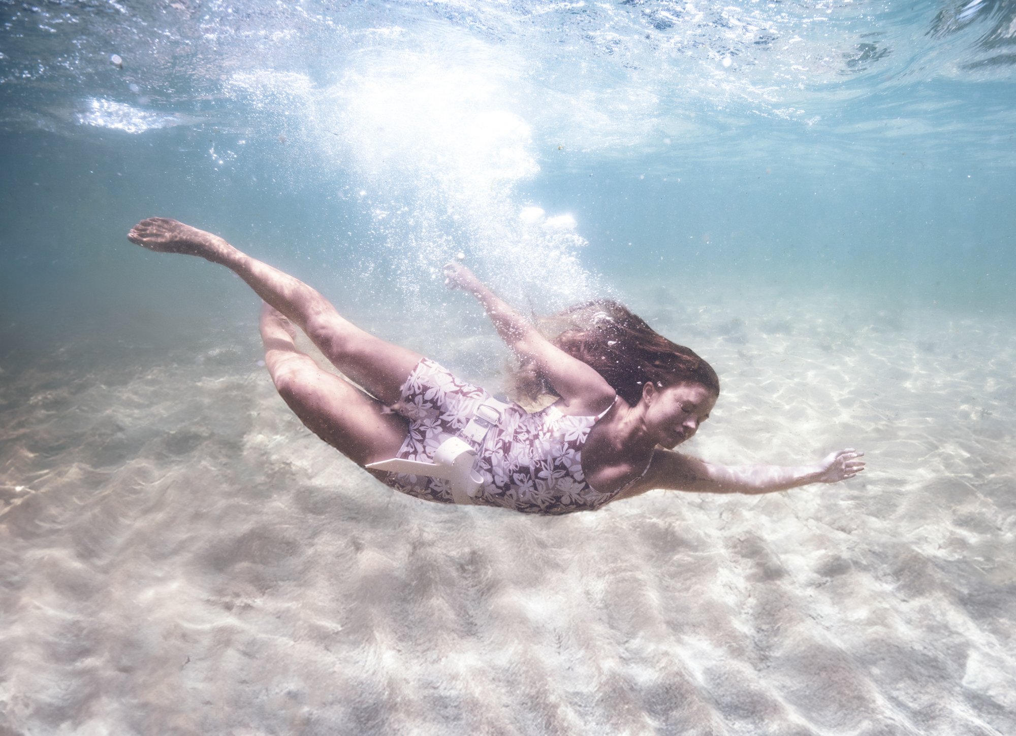 A woman swimming underwater in the ocean, wearing a floral swimsuit, with her hair flowing behind her.