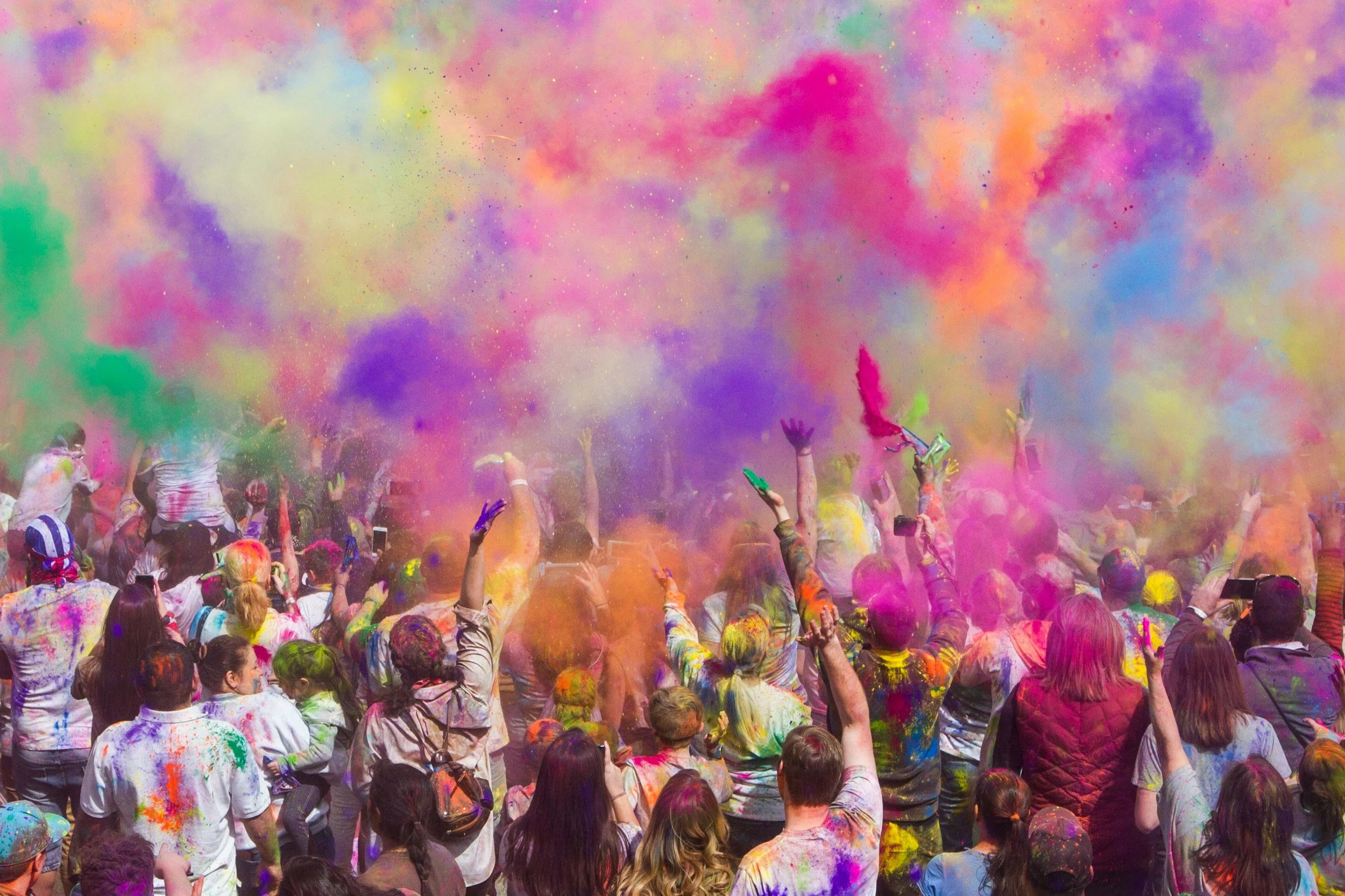 A crowd of people celebrating during a colorful Holi festival, throwing colored powders into the air, creating a vibrant explosion of colors.
