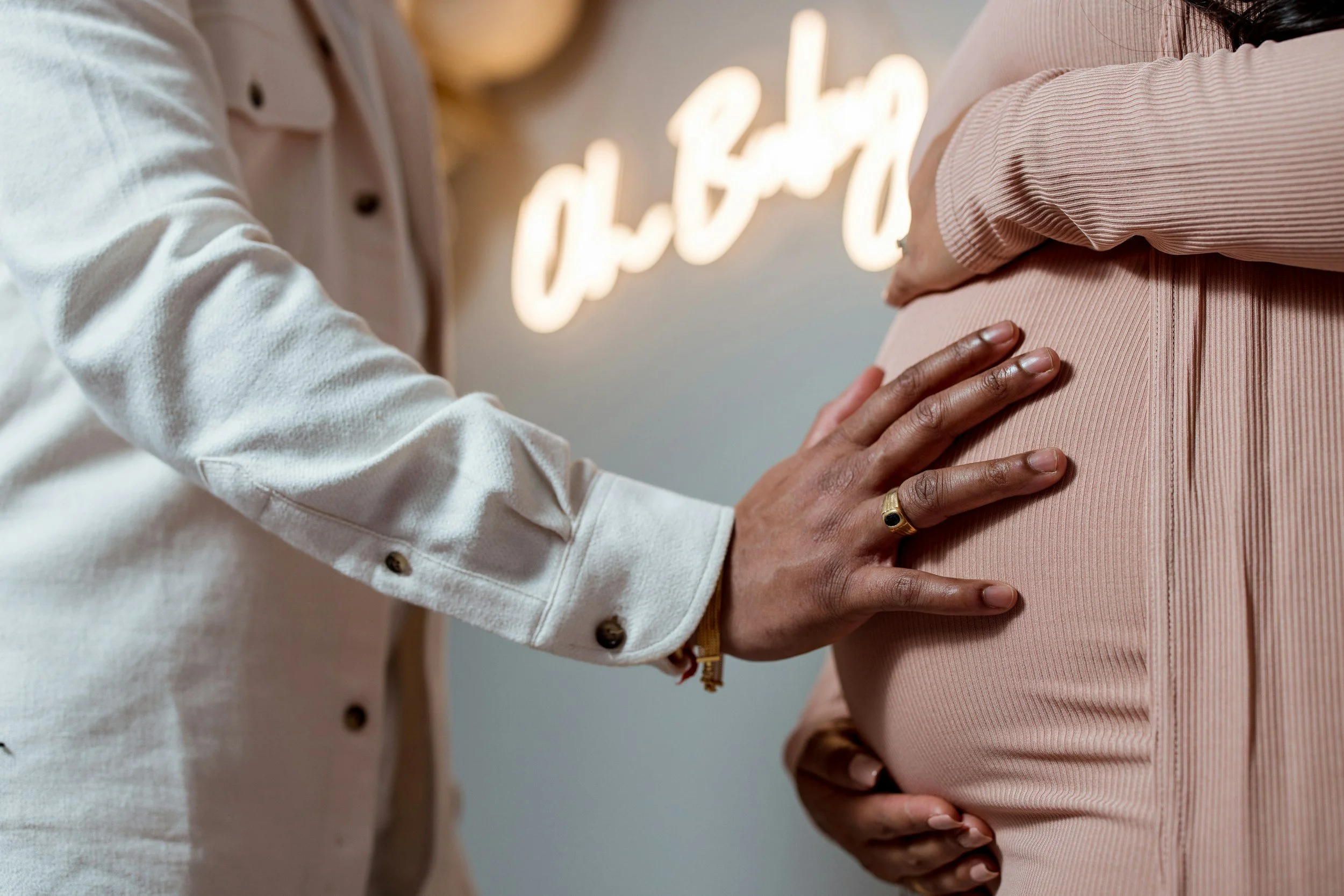 Person's hand gently touching pregnant belly, with a background of illuminated 'Gabe' sign.