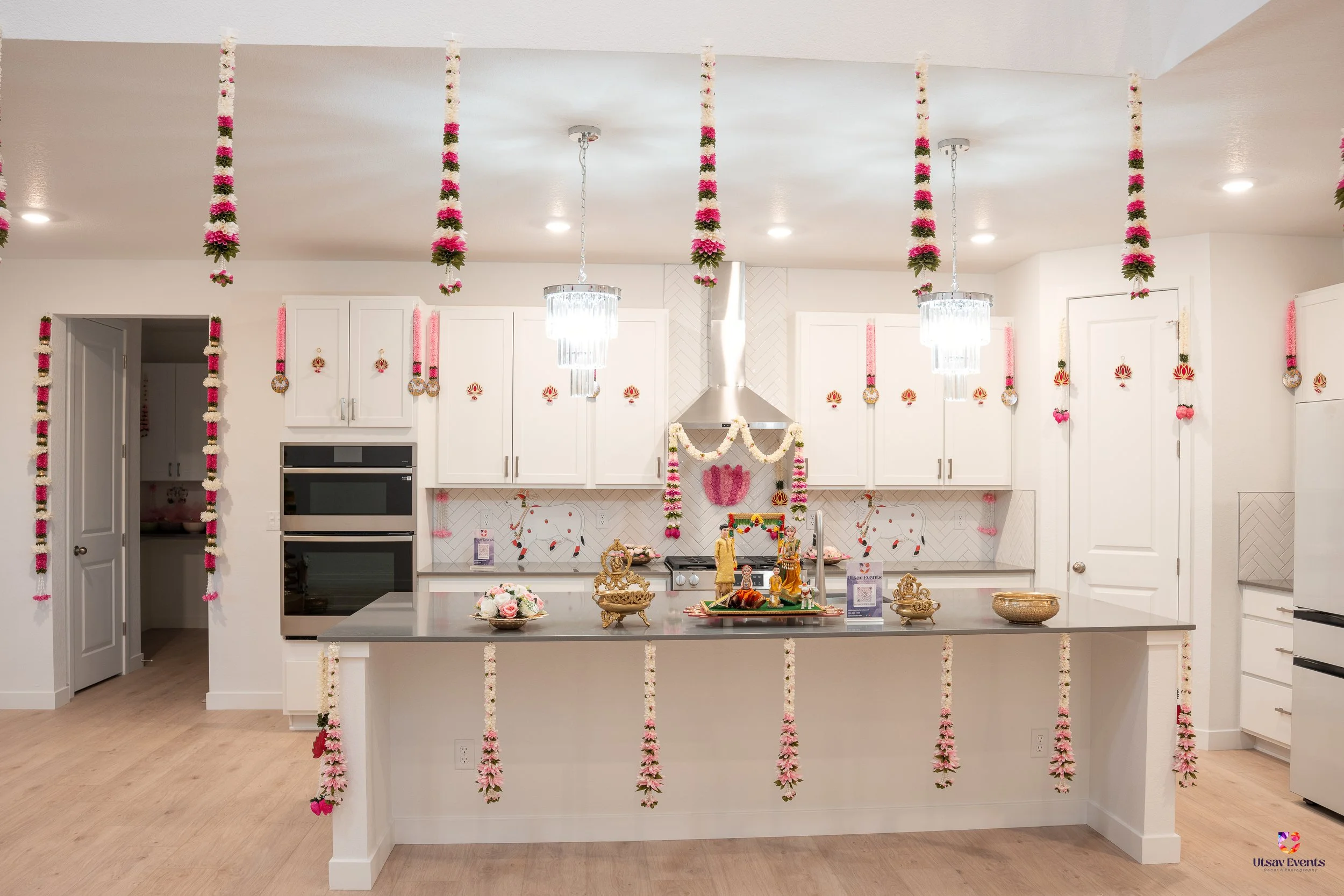 Decorated kitchen with white cabinets and floral garlands hanging from the ceiling, on the island, and around the surroundings, with religious idols and flower arrangements in the center.