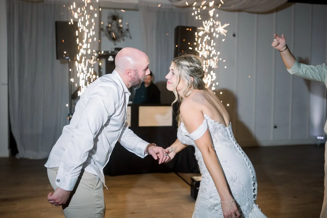 A bride and groom are dancing and holding hands at their wedding reception with sparklers in the background.