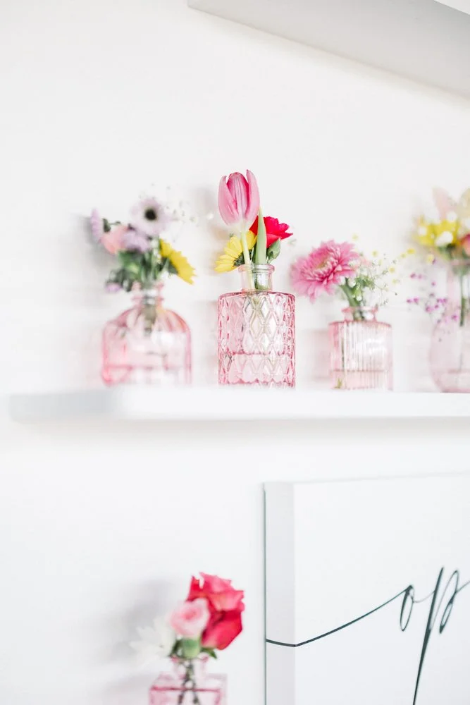 Pink and red wedding flowers in glass bud vases on a white shelf at Granville Farms