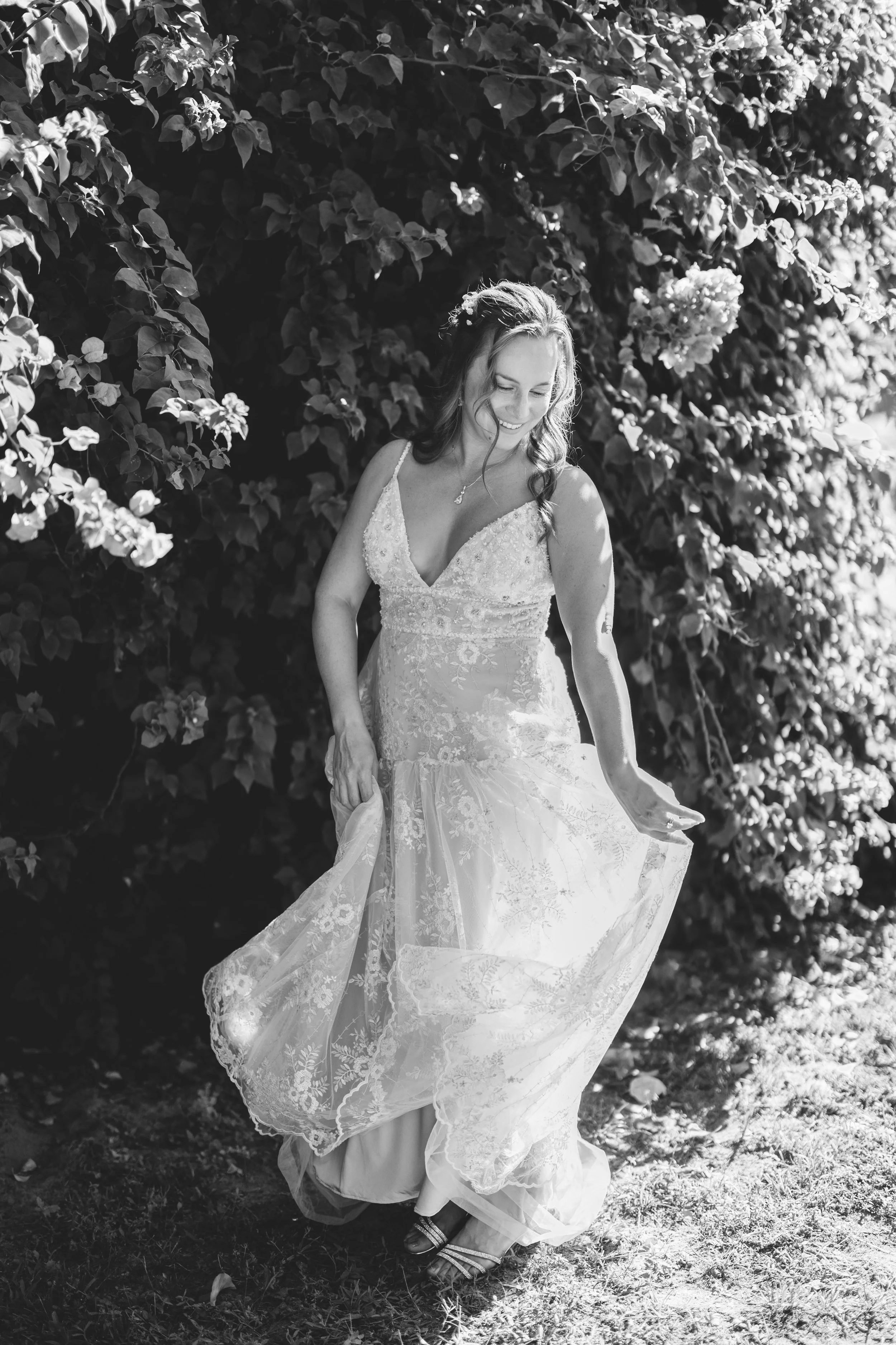 A woman in a wedding dress smiling outdoors near bushes.