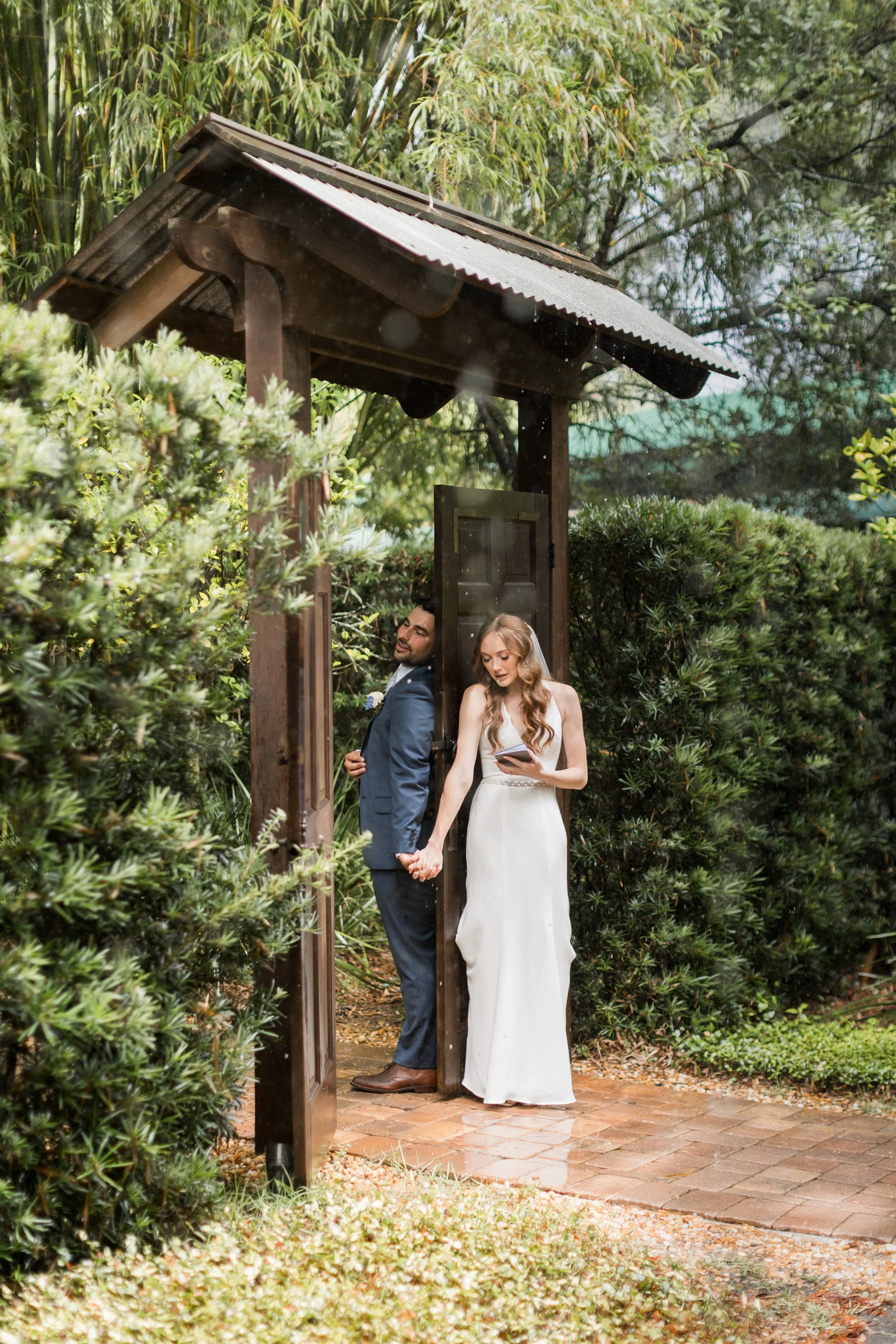 Bride and groom share a first touch at a wooden garden gate at Club Lake wedding venue